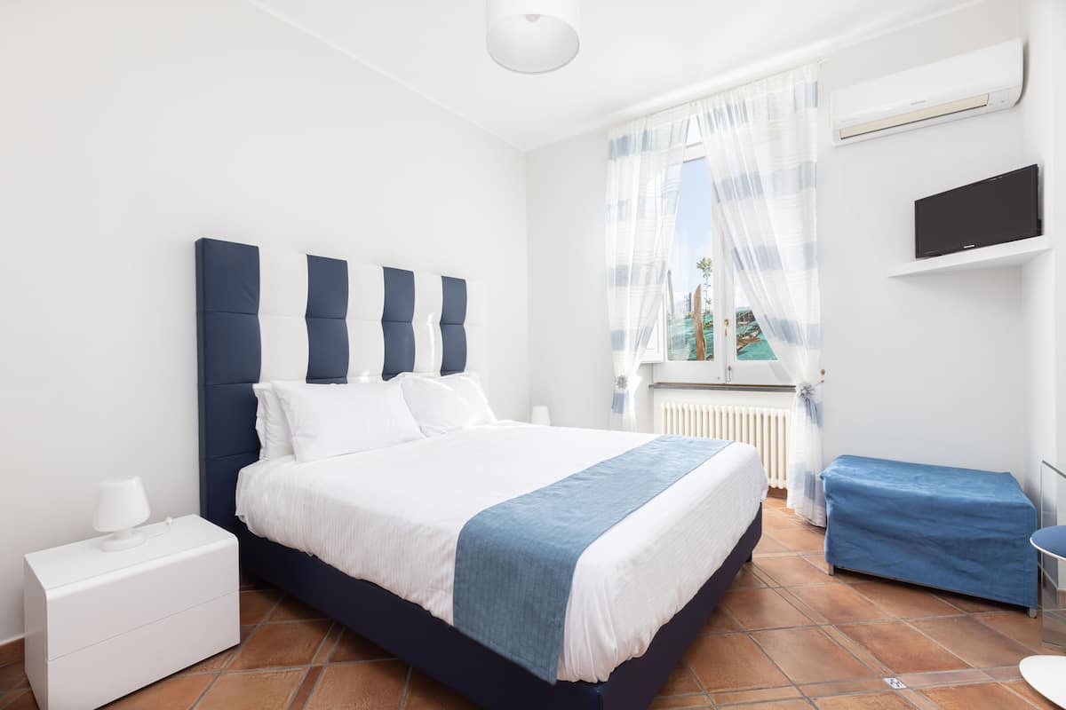 A modern bedroom with a large bed, a bedside table, a TV, and a window with curtains.