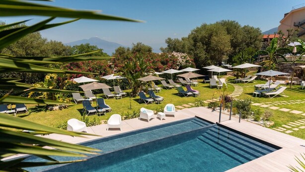 A pool area with lounge chairs and umbrellas, surrounded by greenery and a view of mountains. - Relais Casale Antonietta (Sorrento)
