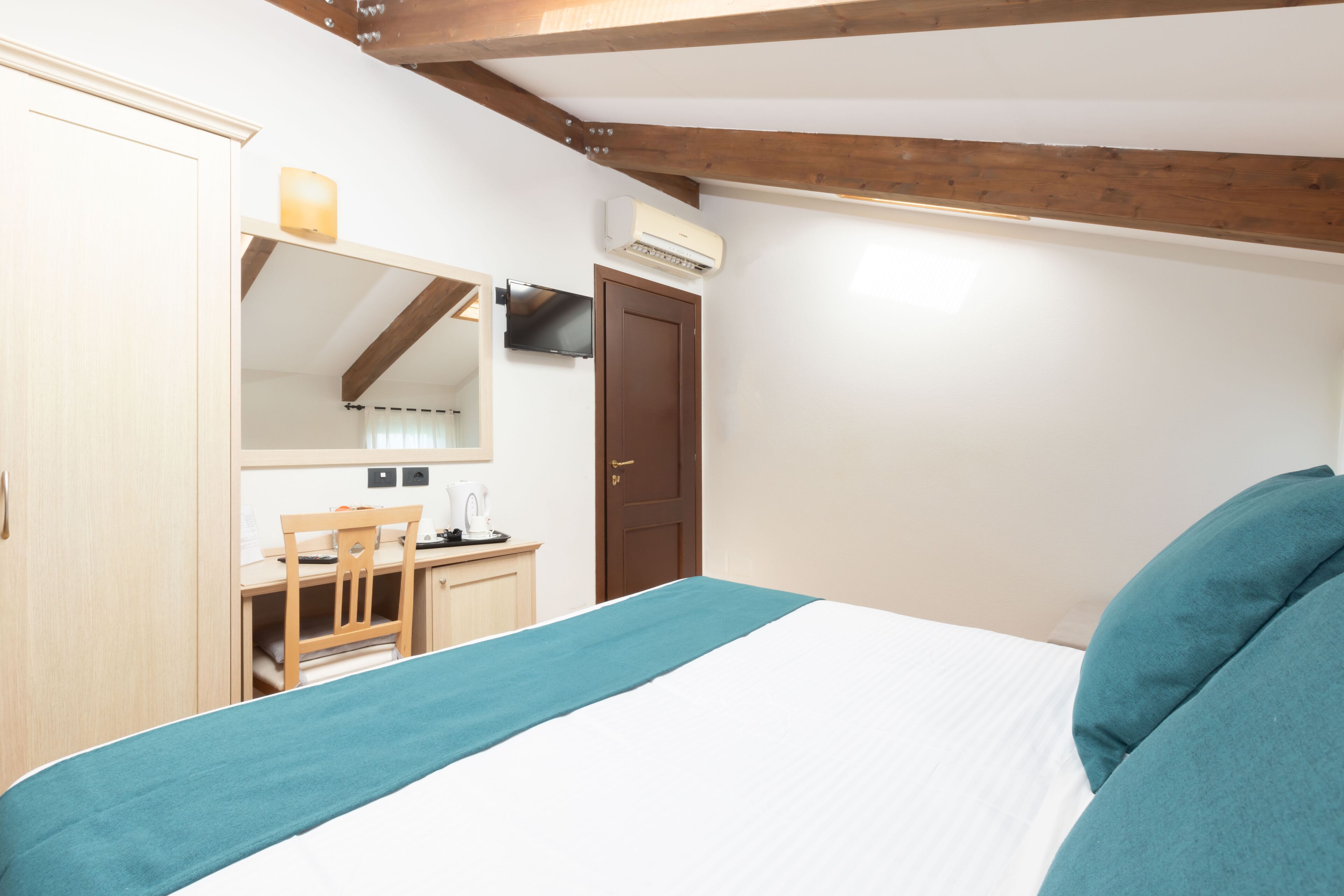 A bedroom with a bed, a desk, a chair, a wardrobe, and an air conditioning unit.