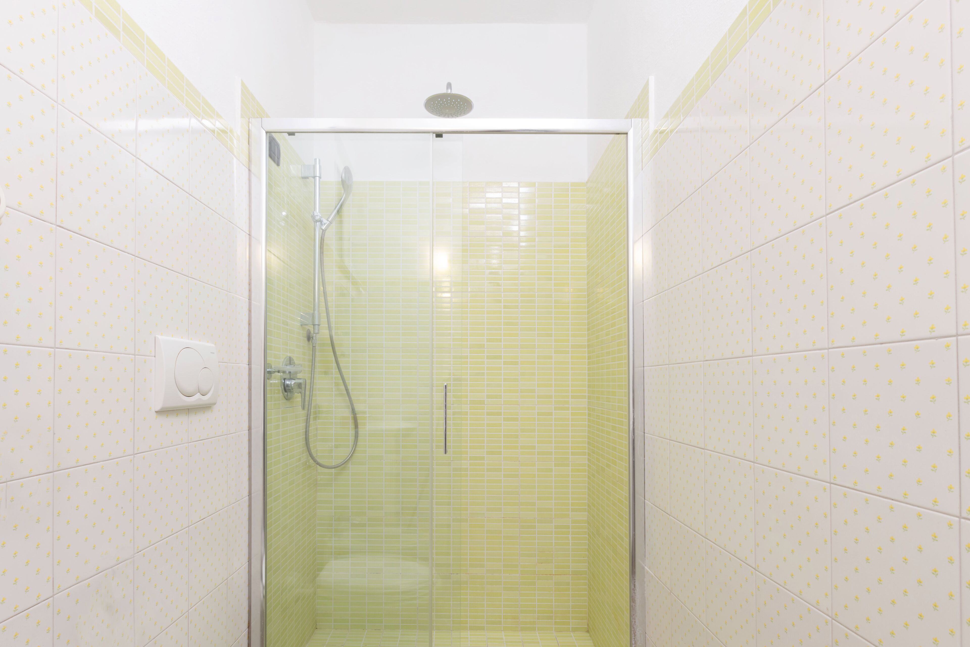 Une douche avec une porte en verre, un pommeau de douche à main et un robinet mural.