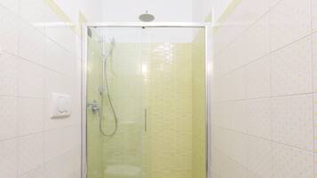 Une douche avec une porte en verre, un pommeau de douche à main et un robinet mural.