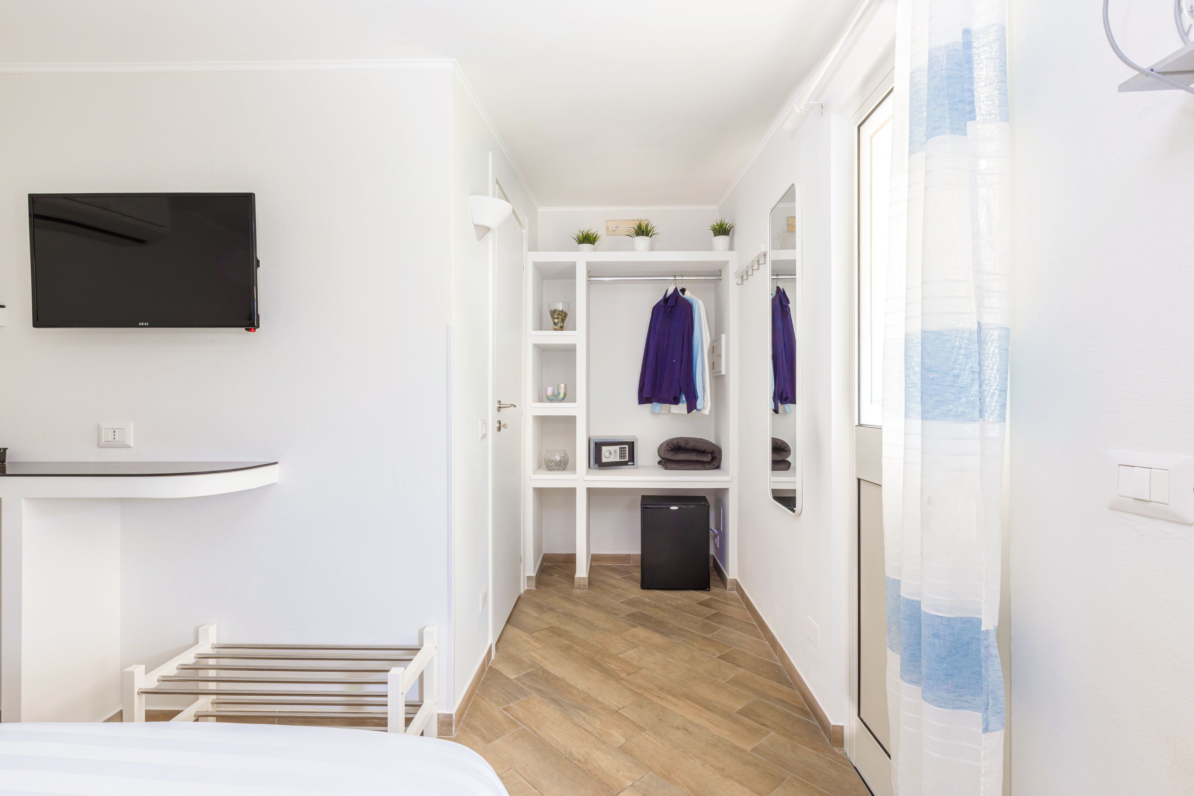 Une chambre d’hôtel comprenant un lit, un téléviseur fixé au mur, un petit bureau, une armoire et un miroir.