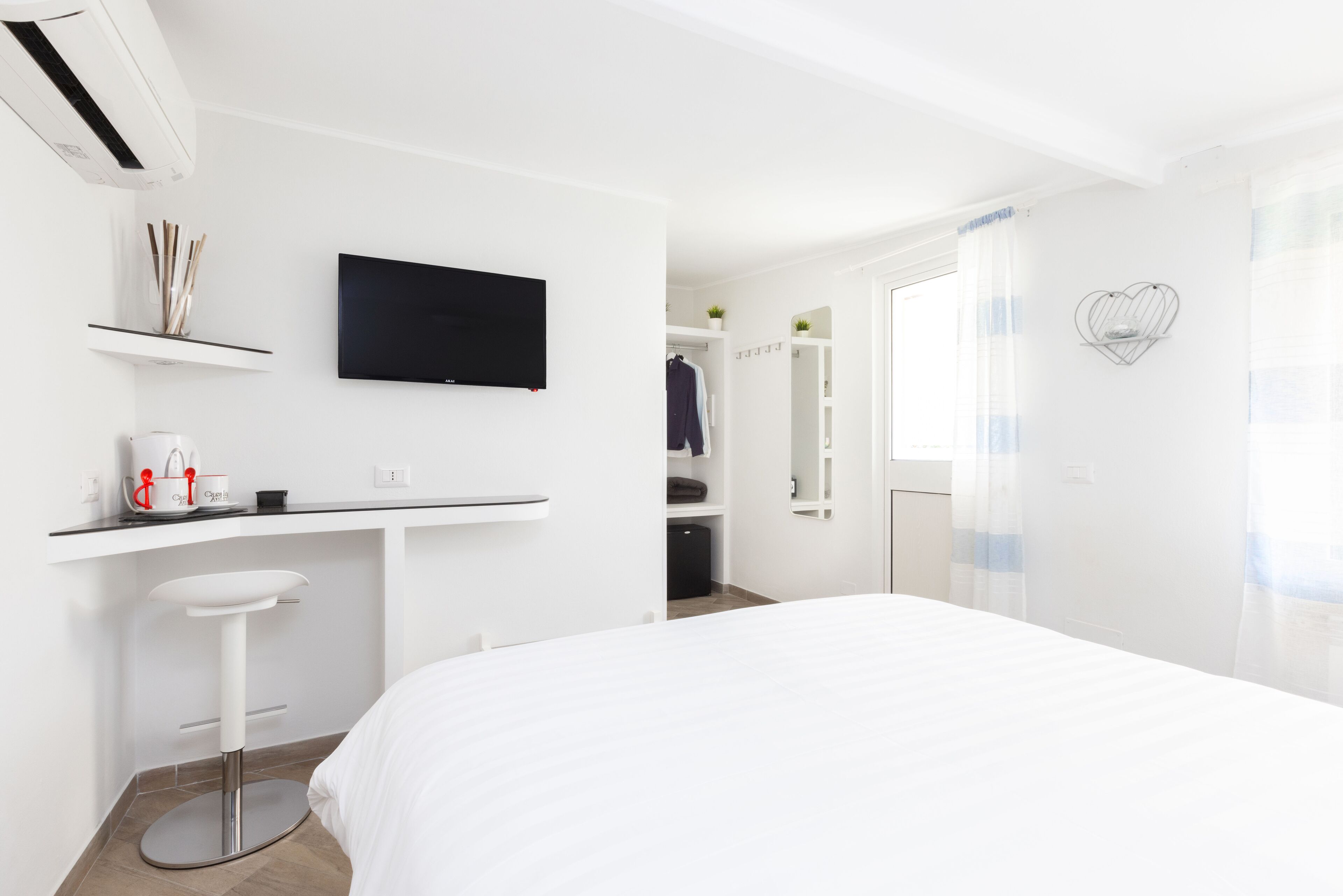 Ein modernes Hotelzimmer mit Bett, weißem Schreibtisch, einem an der Wand montierten Fernseher, einem Badezimmer mit Spiegel und einer Duschkabine.