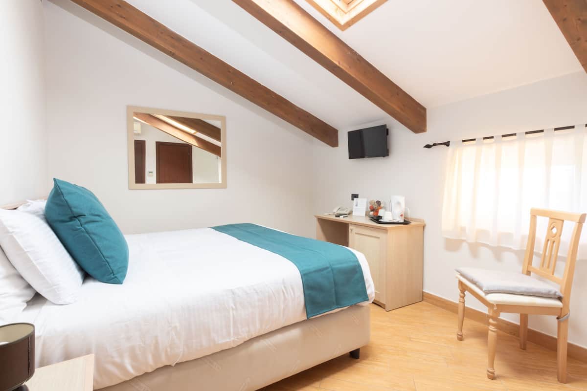 A bedroom with a bed, a chair, a desk, a mirror, and a television.