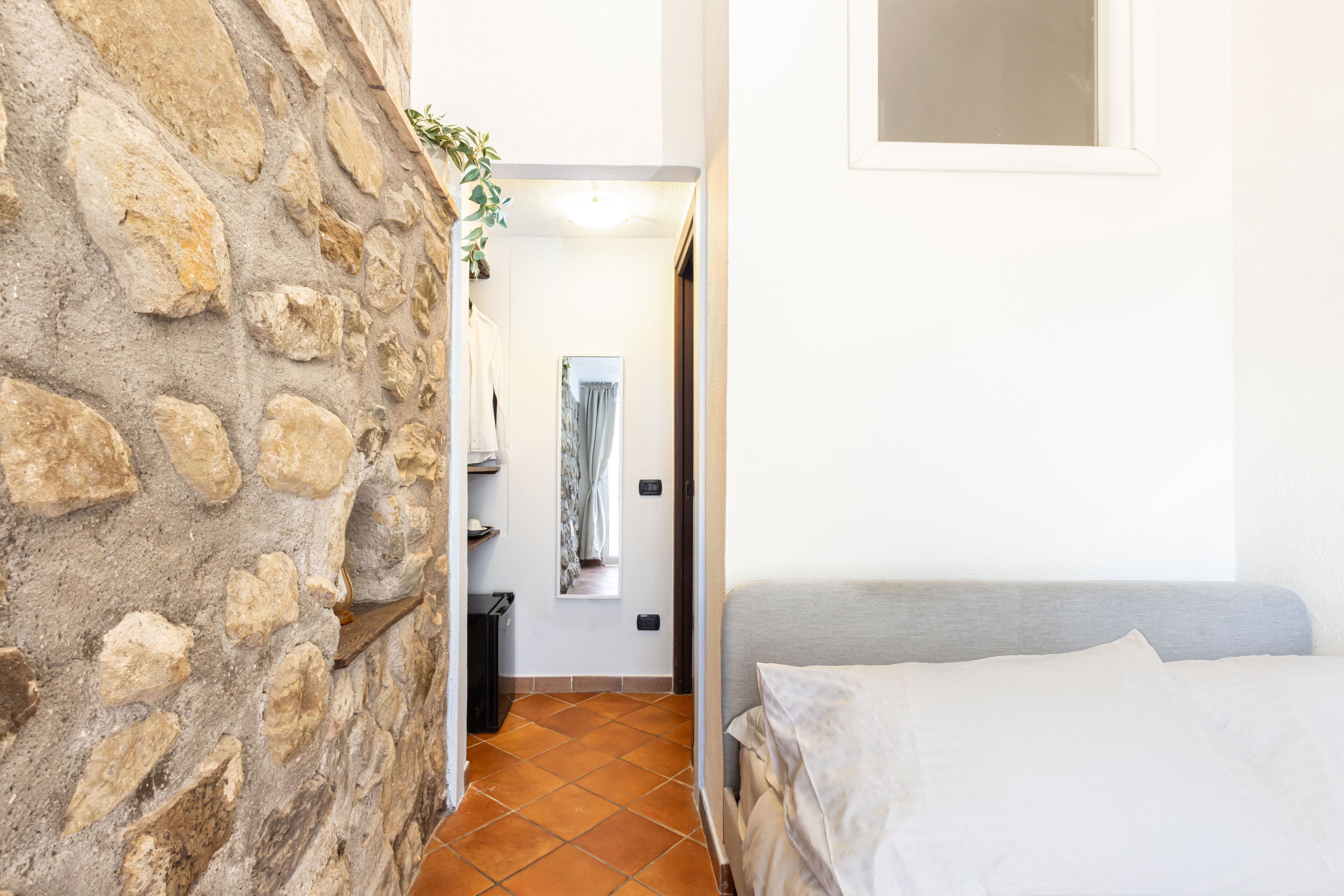 A narrow hallway with a stone wall on one side and a bed with white bedding on the other.