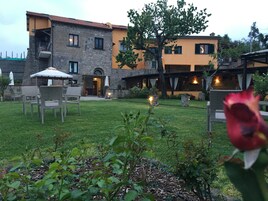 A courtyard with outdoor seating, a stone building with multiple windows, and a tree.