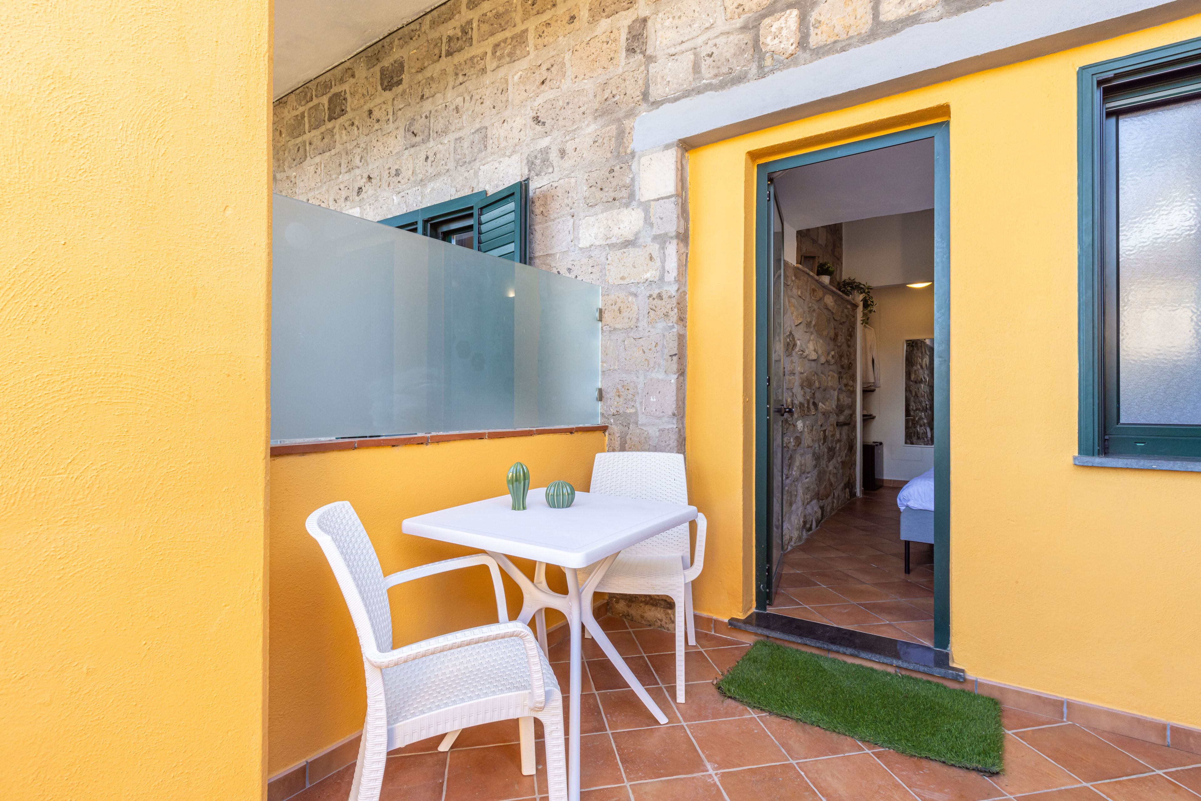 Un petit espace extérieur aménagé avec une table et deux chaises, une porte donnant sur une chambre et un mur en pierre.
