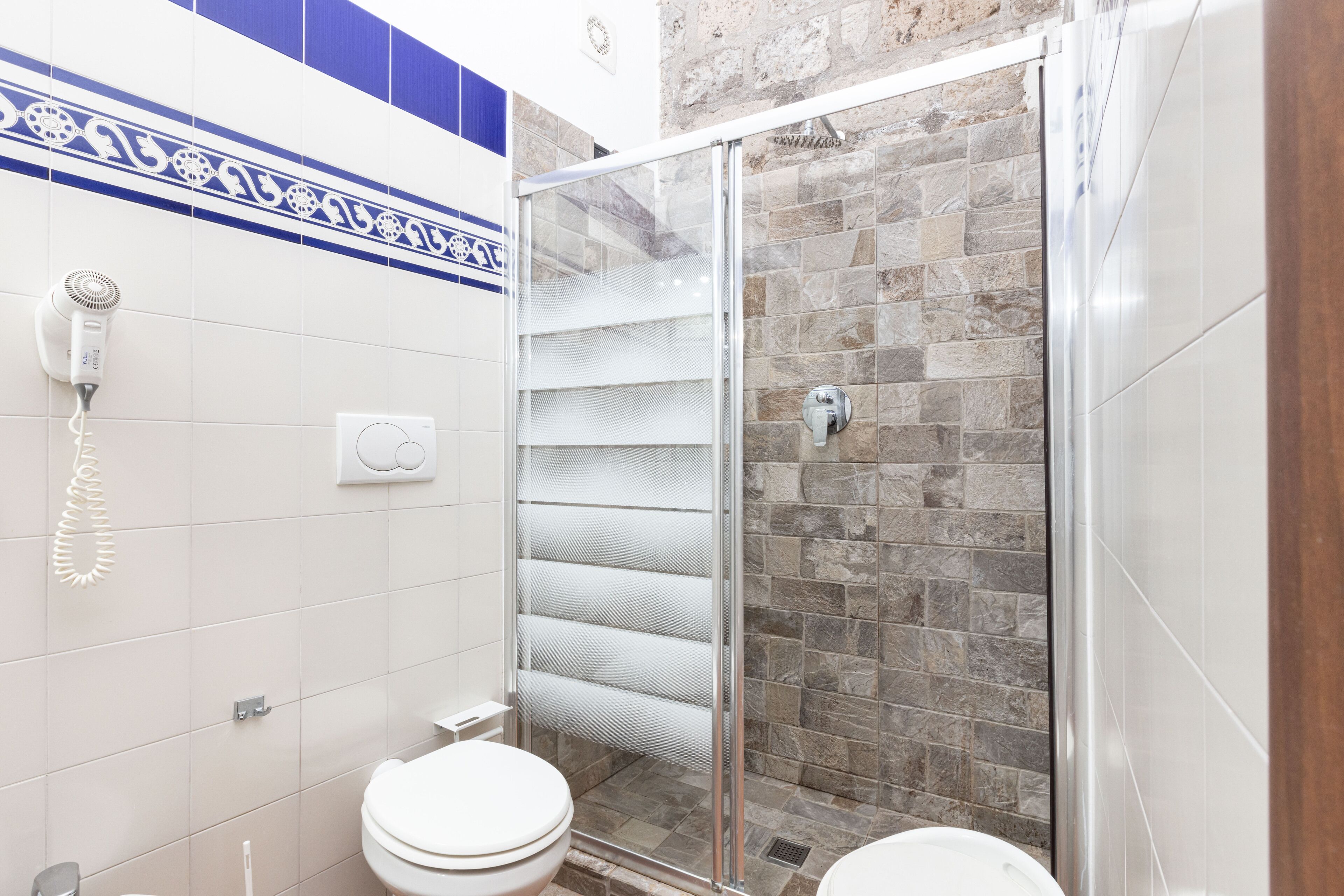 Une salle de bain équipée d’une douche, de toilettes et d’un sèche-cheveux fixé au mur.