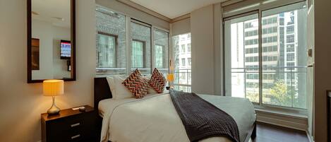 Une chambre d’hôtel moderne, dotée d’un grand lit, d’une table de chevet, d’une lampe et d’une grande fenêtre donnant sur la ville.