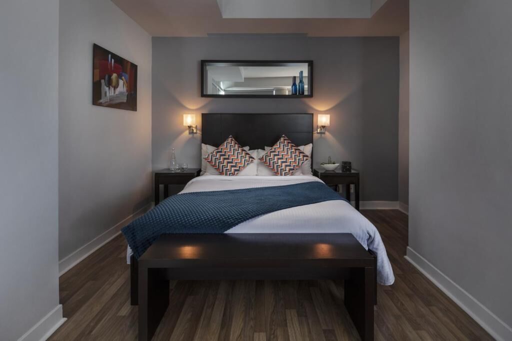 Een moderne slaapkamer met een donker hoofdbord, twee nachtkastjes, een groot bed met gekleurde kussens en een wandspiegel.