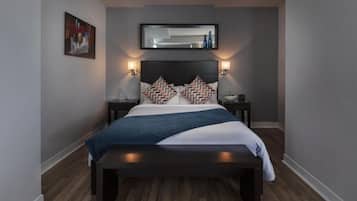Een moderne slaapkamer met een donker hoofdbord, twee nachtkastjes, een groot bed met gekleurde kussens en een wandspiegel.