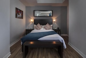 Een moderne slaapkamer met een donker hoofdbord, twee nachtkastjes, een groot bed met gekleurde kussens en een wandspiegel.