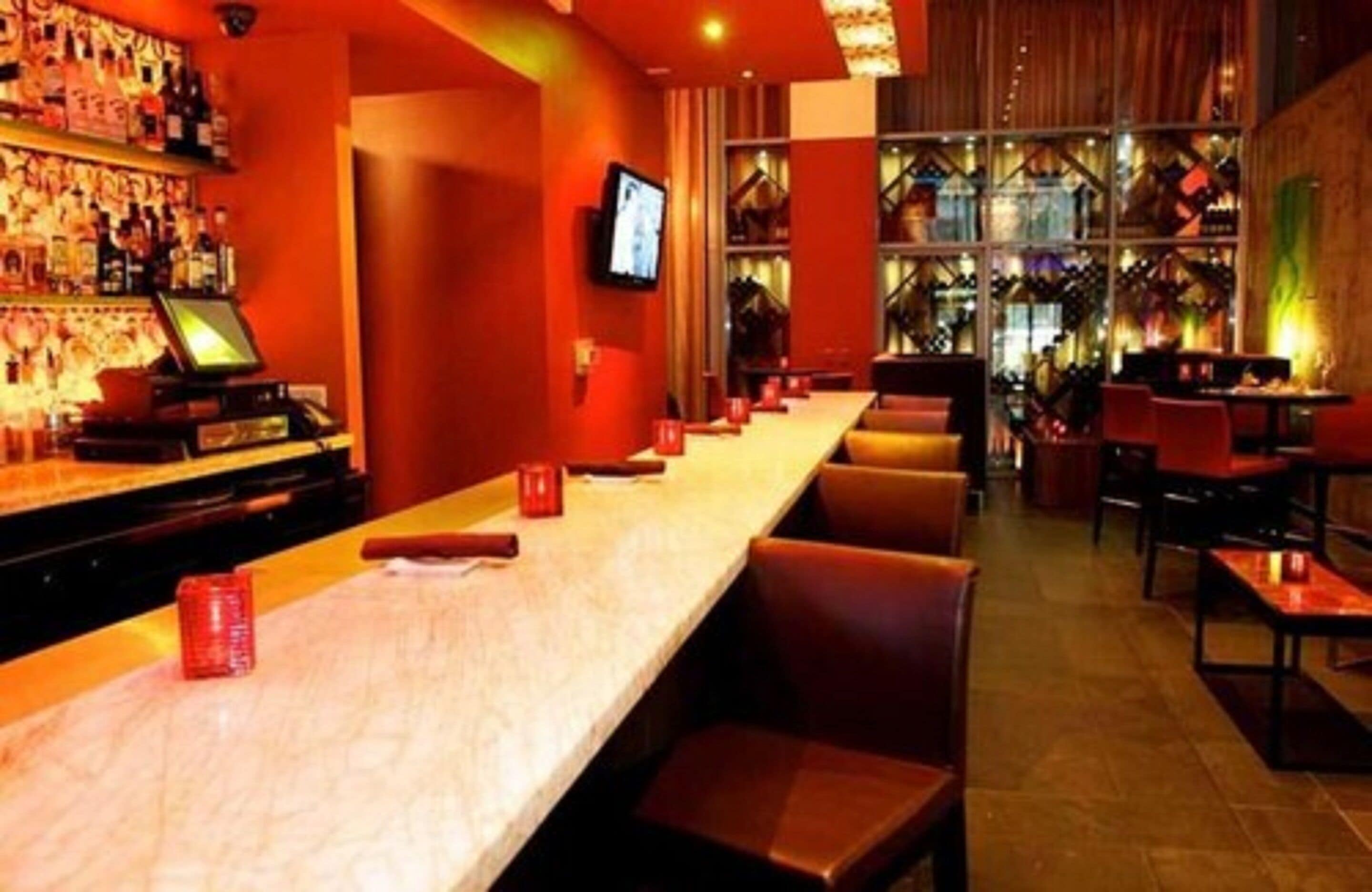 Una zona de bar con una barra alargada, diversas opciones de asientos y una pantalla de televisión en la pared.