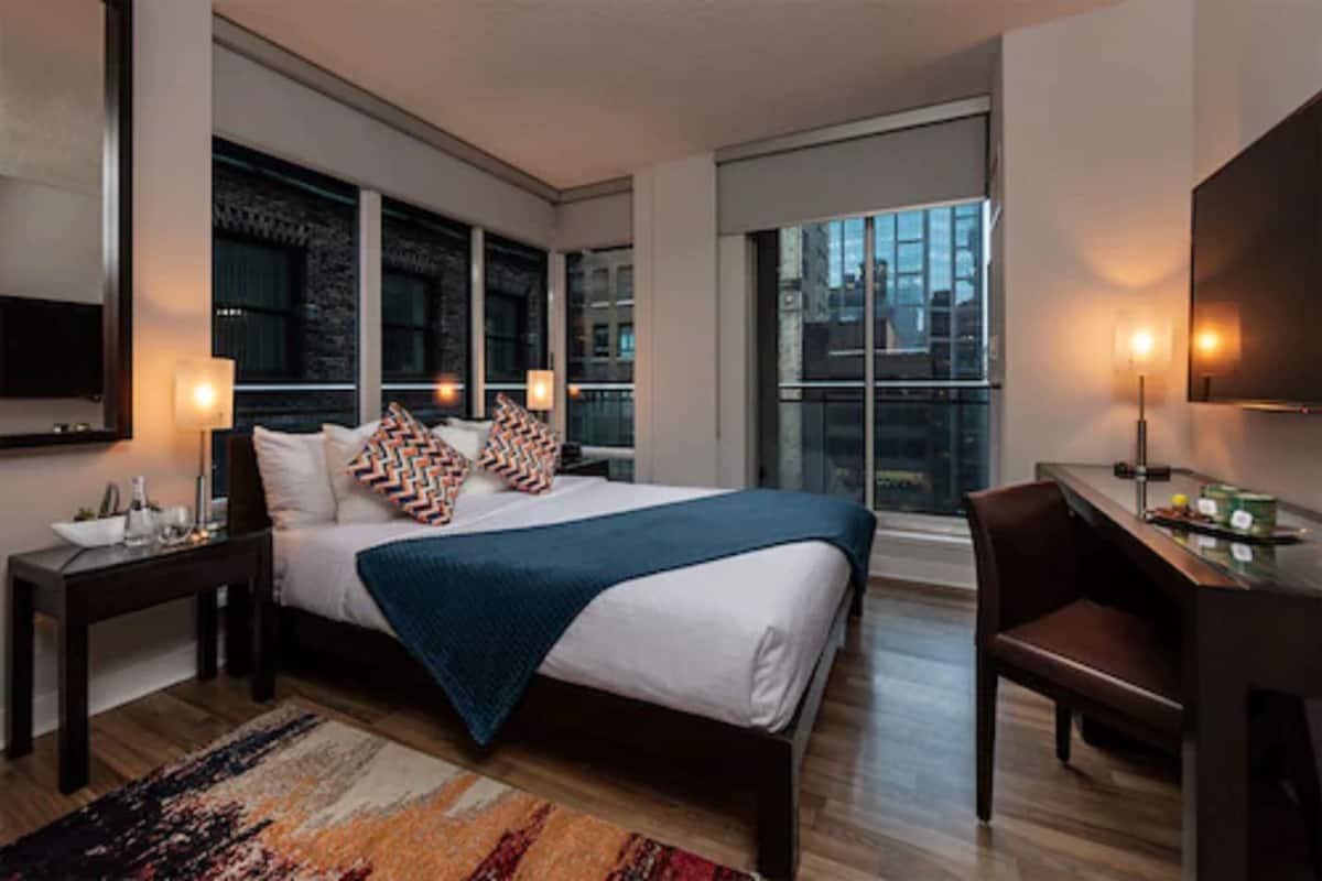 Ein modernes Hotelzimmer mit einem großen Bett, einem Schreibtisch und Blick auf die Stadt durch große Fenster.