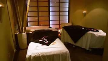 Two beds with white linens and black blankets, a small table, and a vase with flowers.
