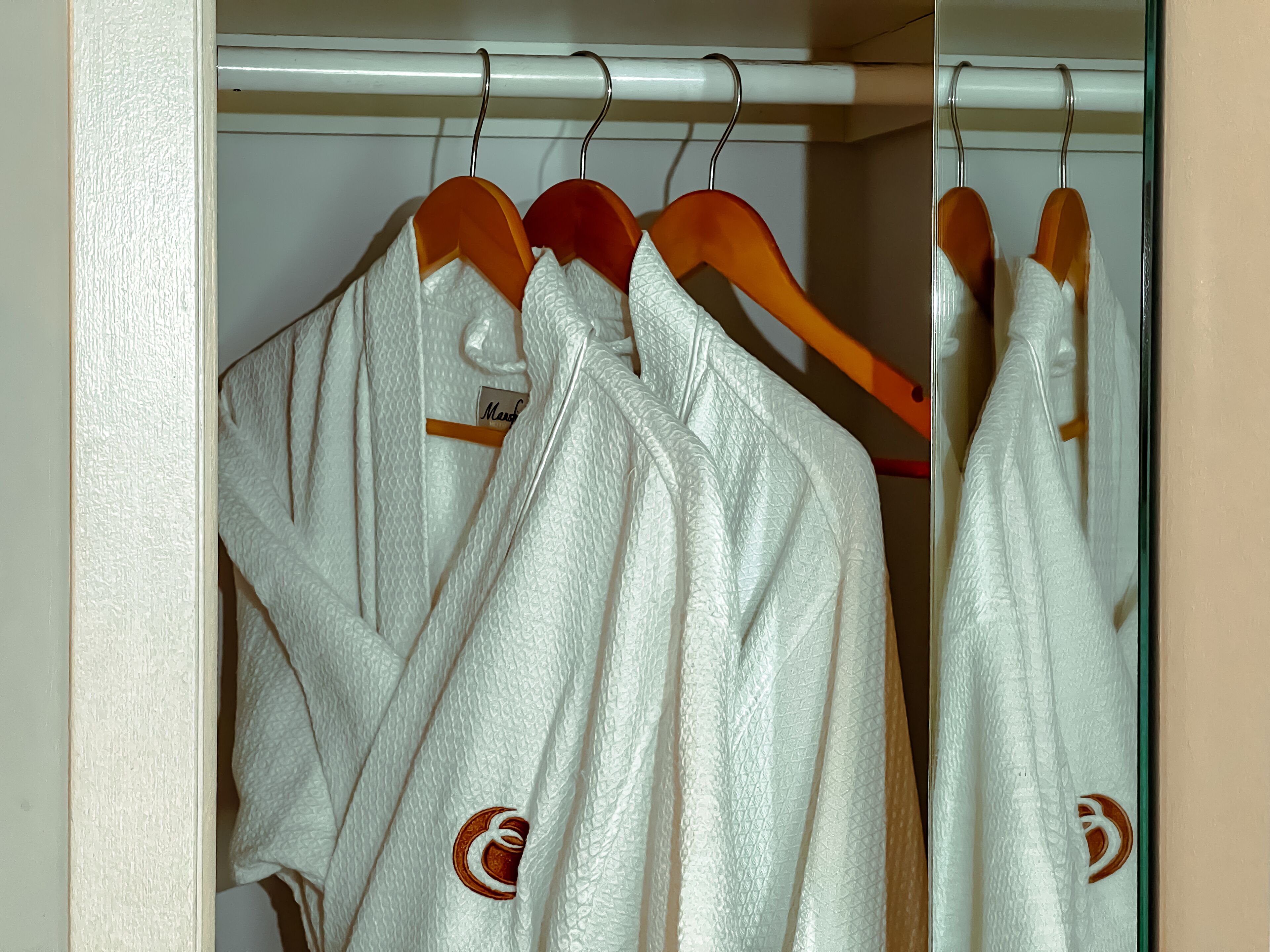 Un armadio con accappatoi bianchi e strutturati appesi a grucce di legno.