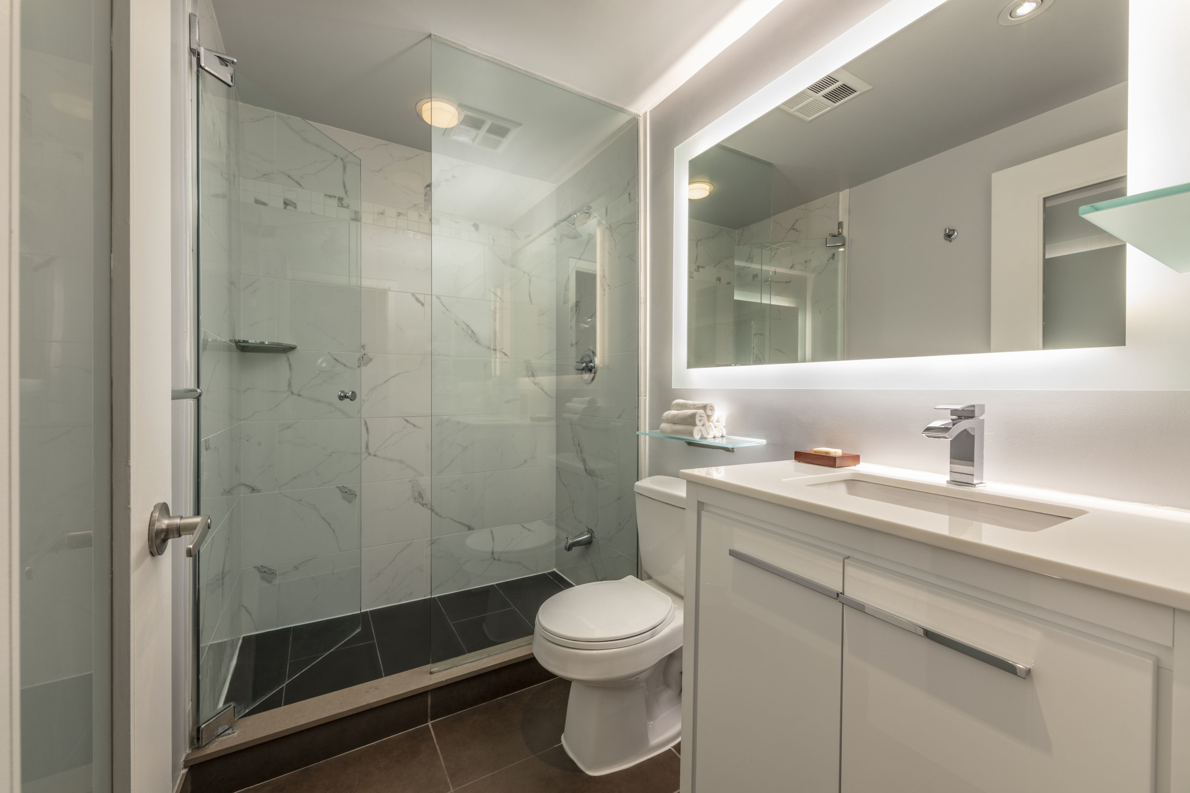 Un baño moderno con ducha de vidrio, inodoro blanco y tocador con espejo.