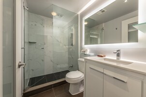 Un baño moderno con ducha de vidrio, inodoro blanco y tocador con espejo.