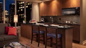 Una cocina moderna con barra, ventanas amplias con vista a la ciudad y un rincón acogedor con sofá y mesa de centro.