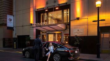 Een hotel ingang met een bord waarop 'Cosmopolitan' staat, en een man en vrouw die een zwarte auto verlaten.