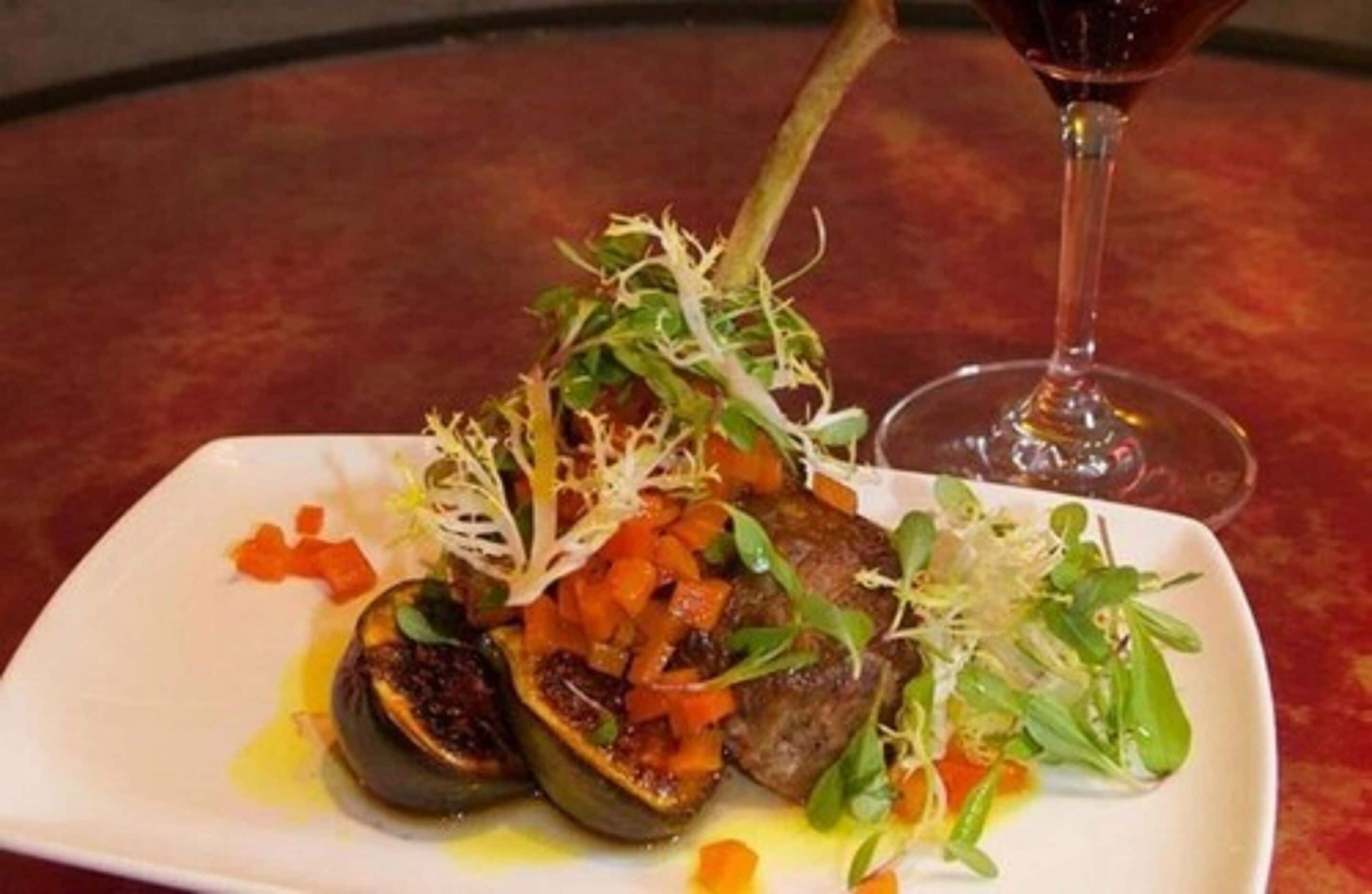A plate of food with a glass of red wine on a table.