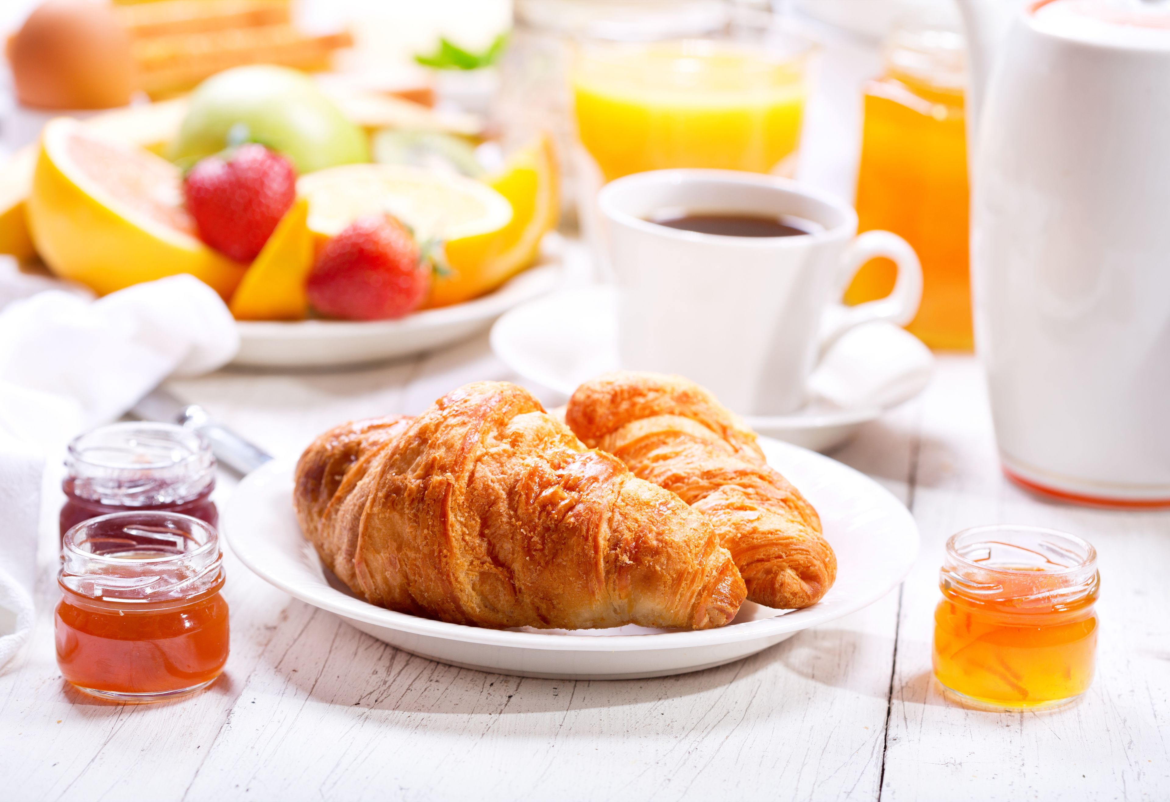 A breakfast setting with croissants, fruit, coffee, and honey jars.