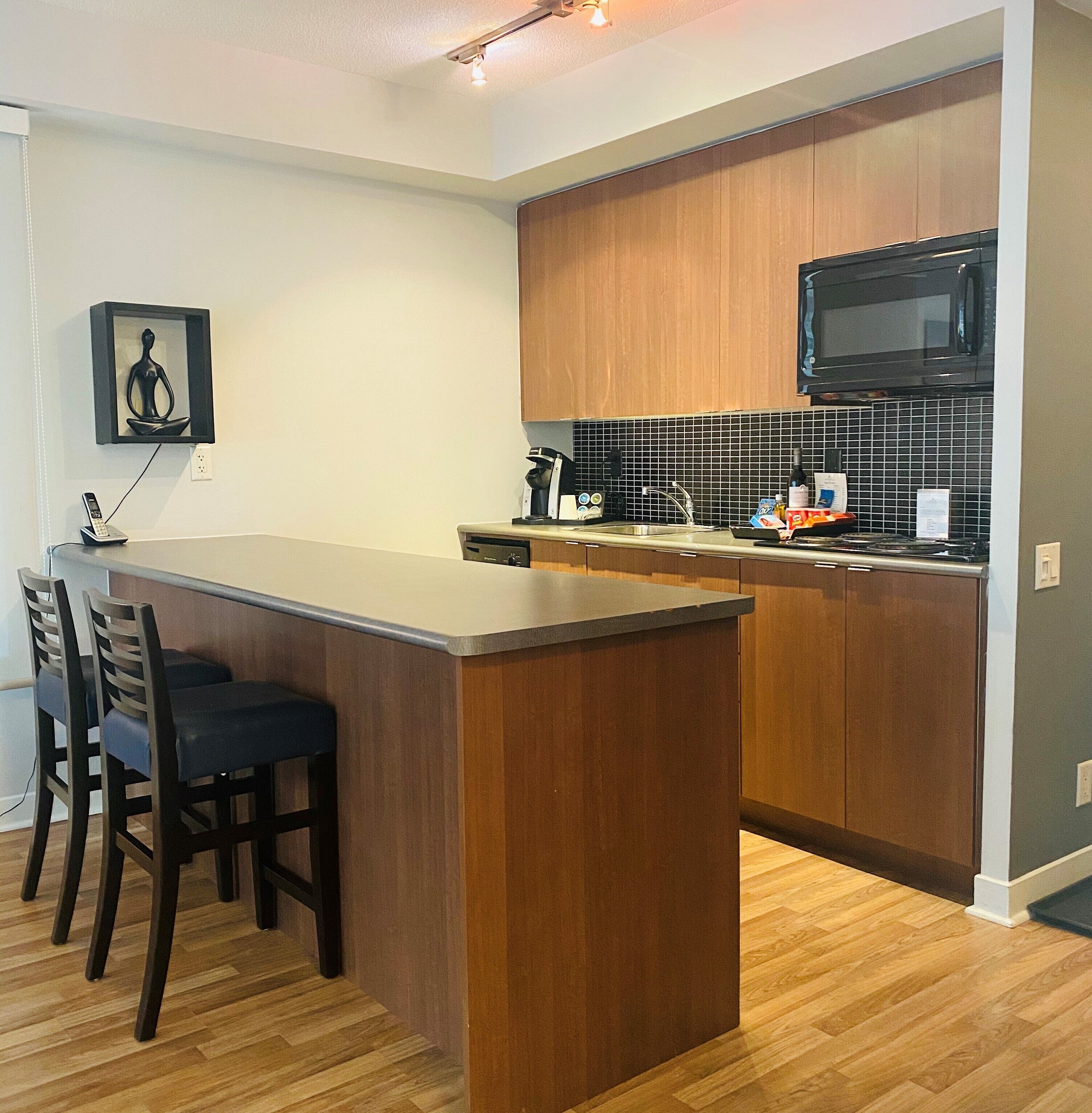 Una cocina moderna con una isla de madera, taburetes de bar, microondas y salpicadero de azulejos.