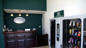 A hotel reception area with a dark wood counter, a sign reading "Empire", and a vending machine stocked with snacks.