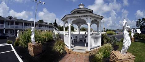 A gazebo with a white roof and columns, surrounded by stone planters and statues.