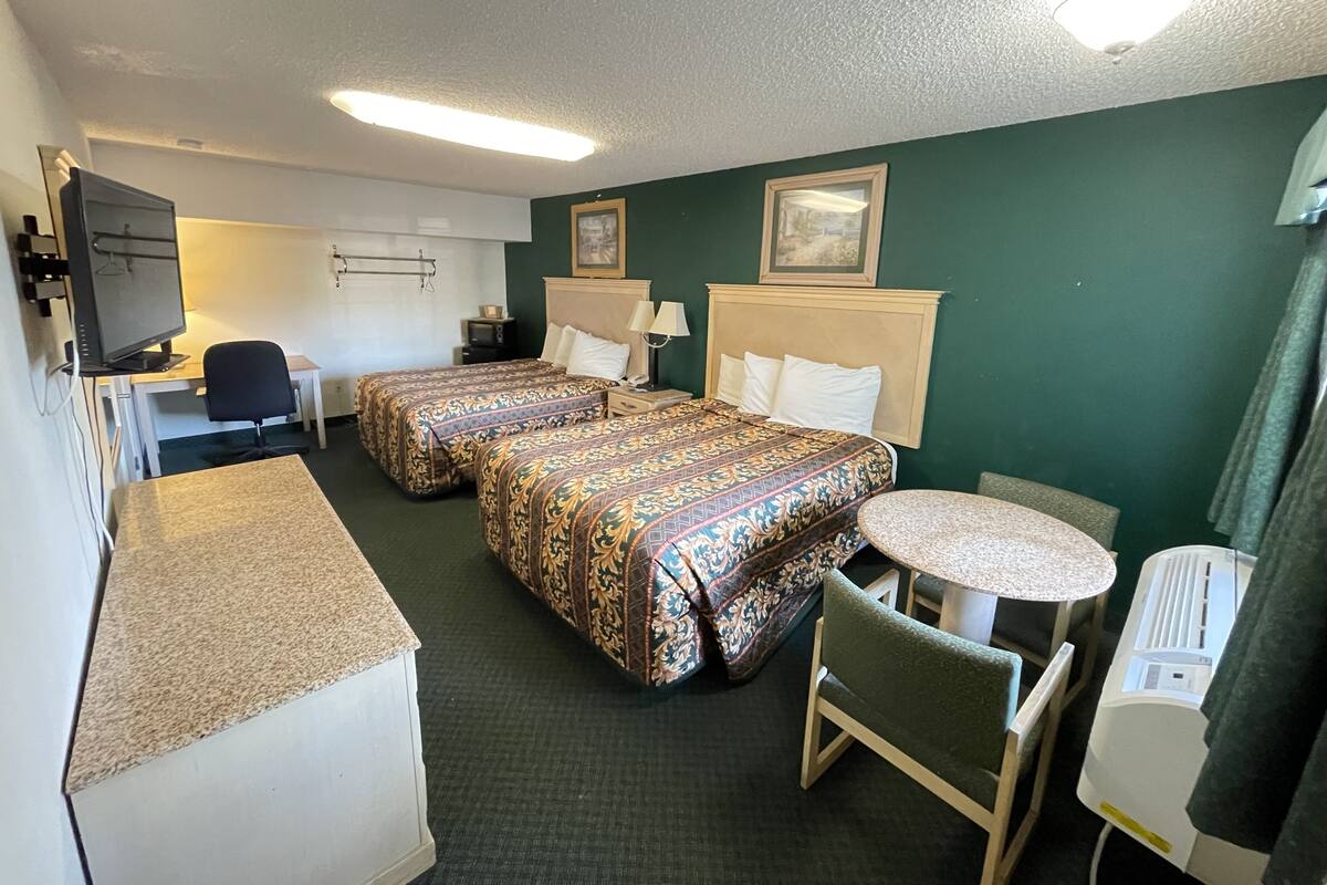 A hotel room with two beds, a desk, a chair, a small table, a television, and a heater.