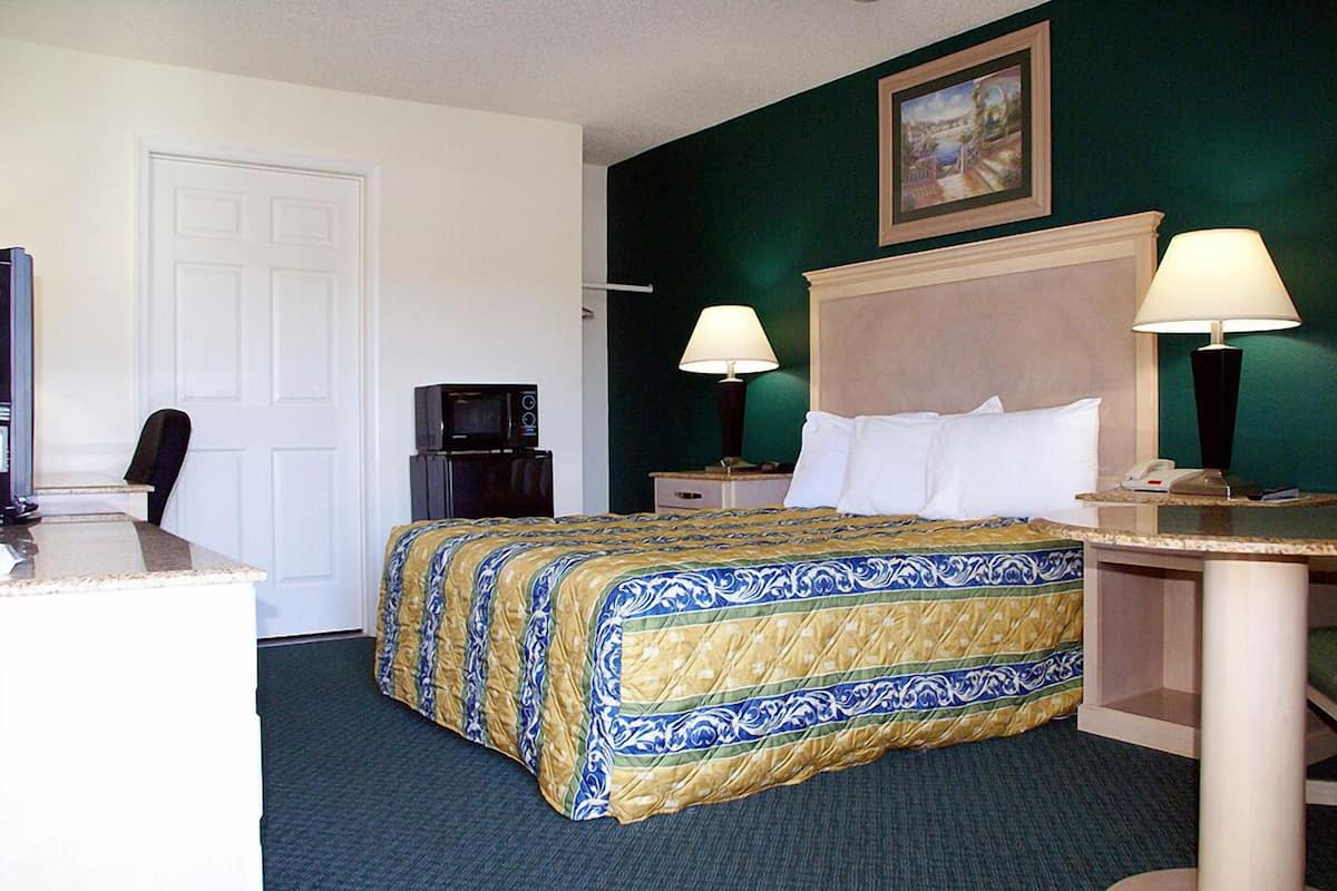 A hotel room with a bed, two bedside lamps, a desk with a telephone, a television, and a door.