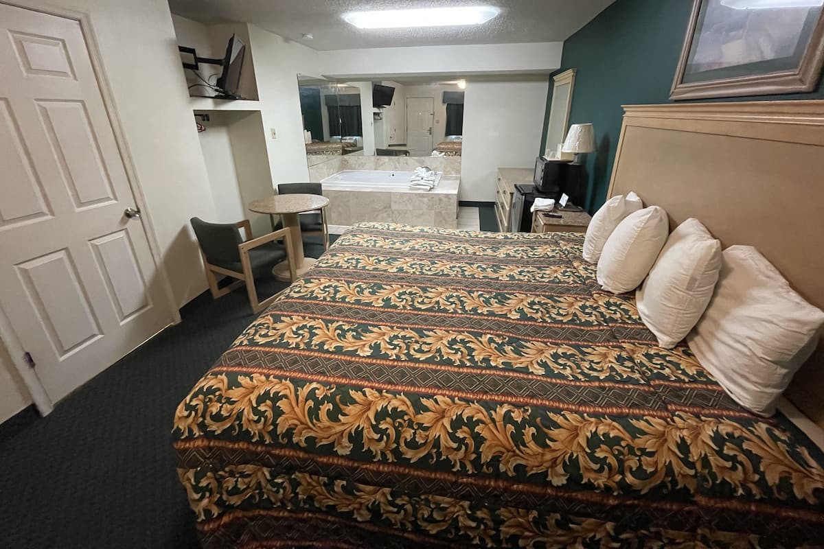 A hotel room with a large bed, a desk, a chair, a bathroom with a bathtub, and a television.