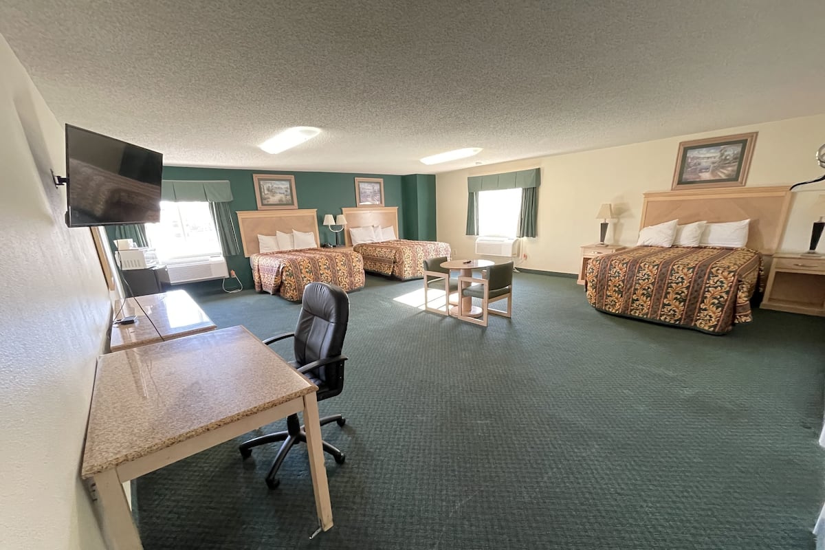 A hotel room with two beds, a desk with a chair, a flat-screen TV, and a window with curtains.