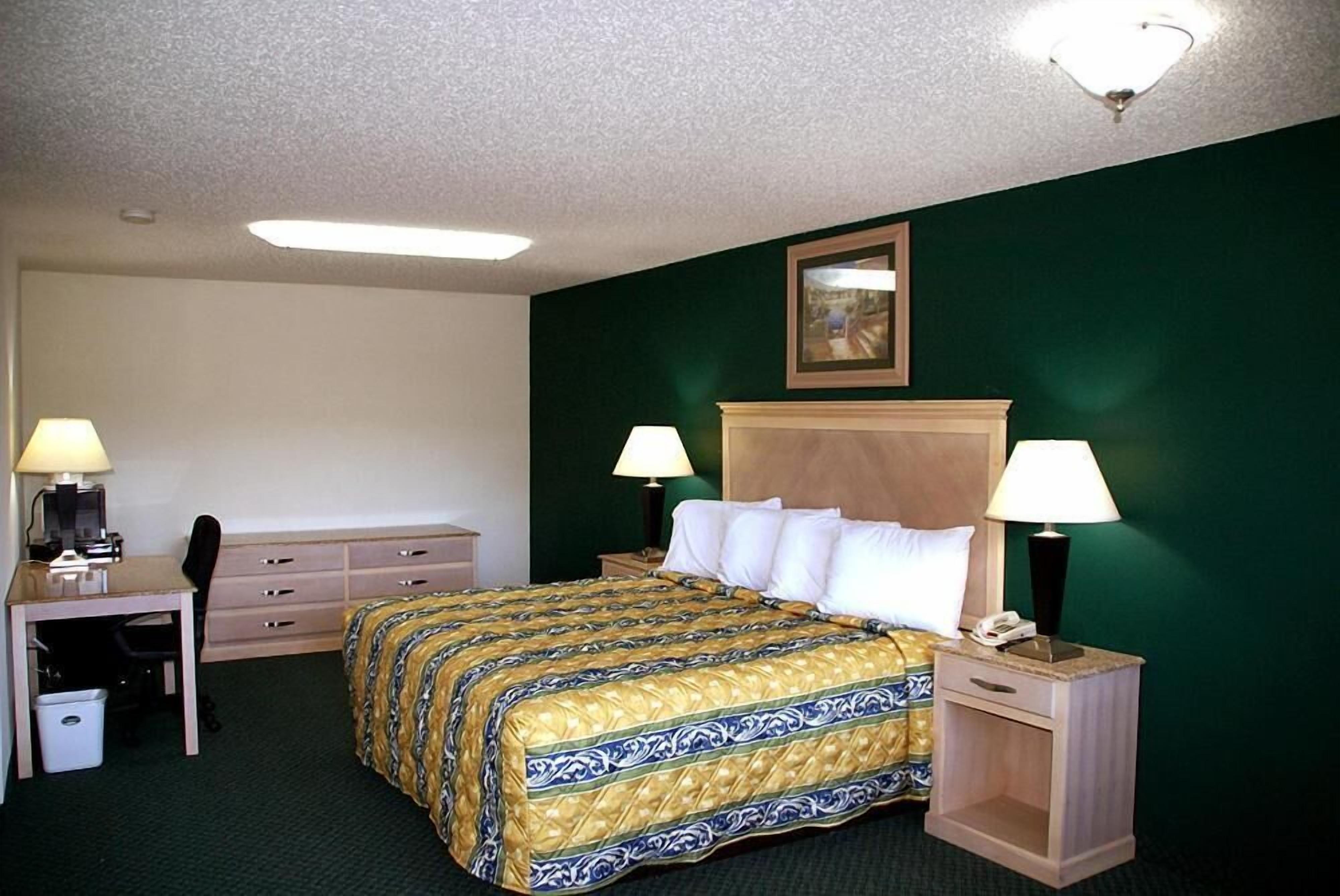 A hotel room with a bed, desk, chair, and two bedside lamps.