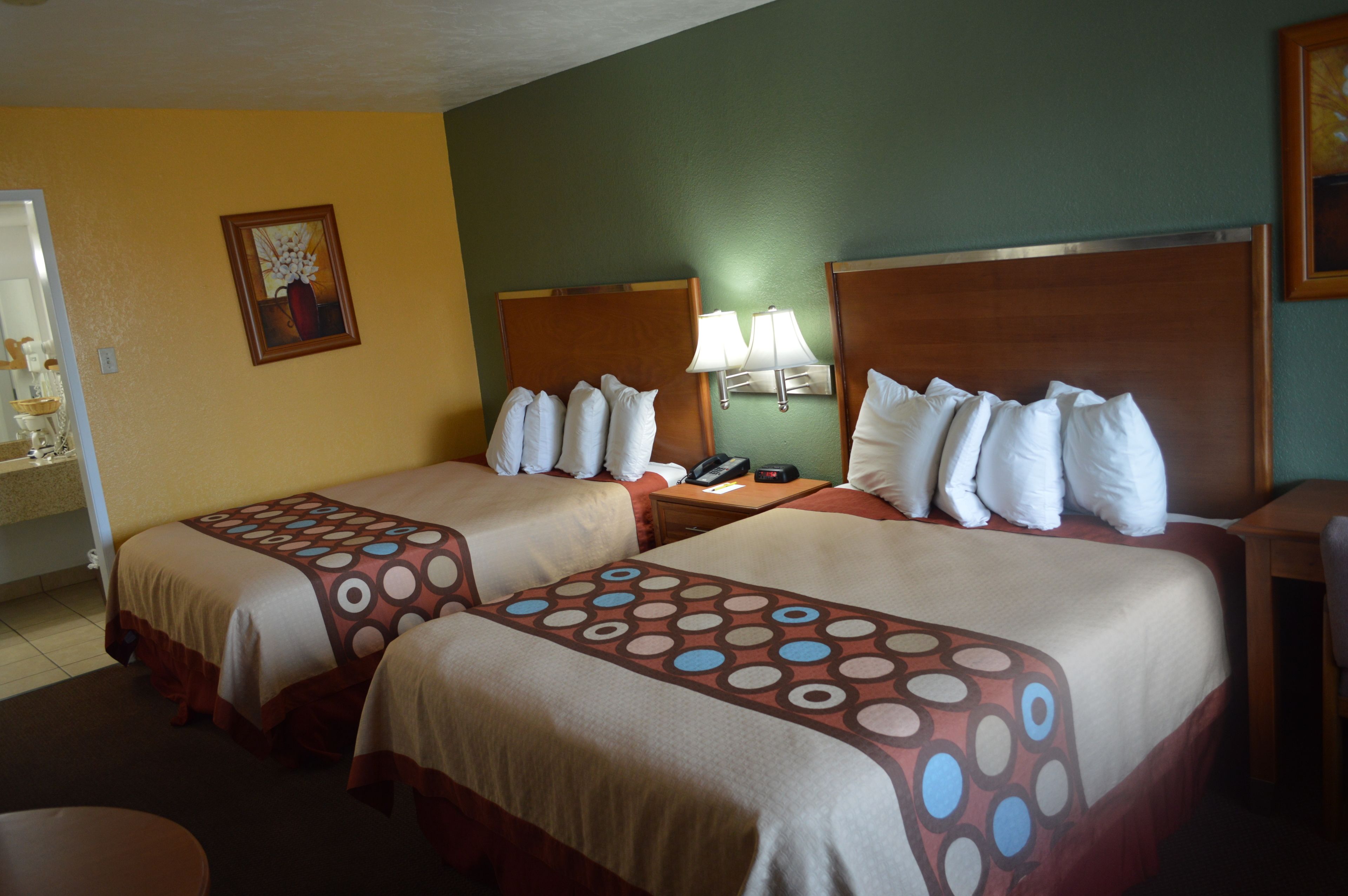 A hotel room with two beds, a nightstand with a lamp, and a painting on the wall.