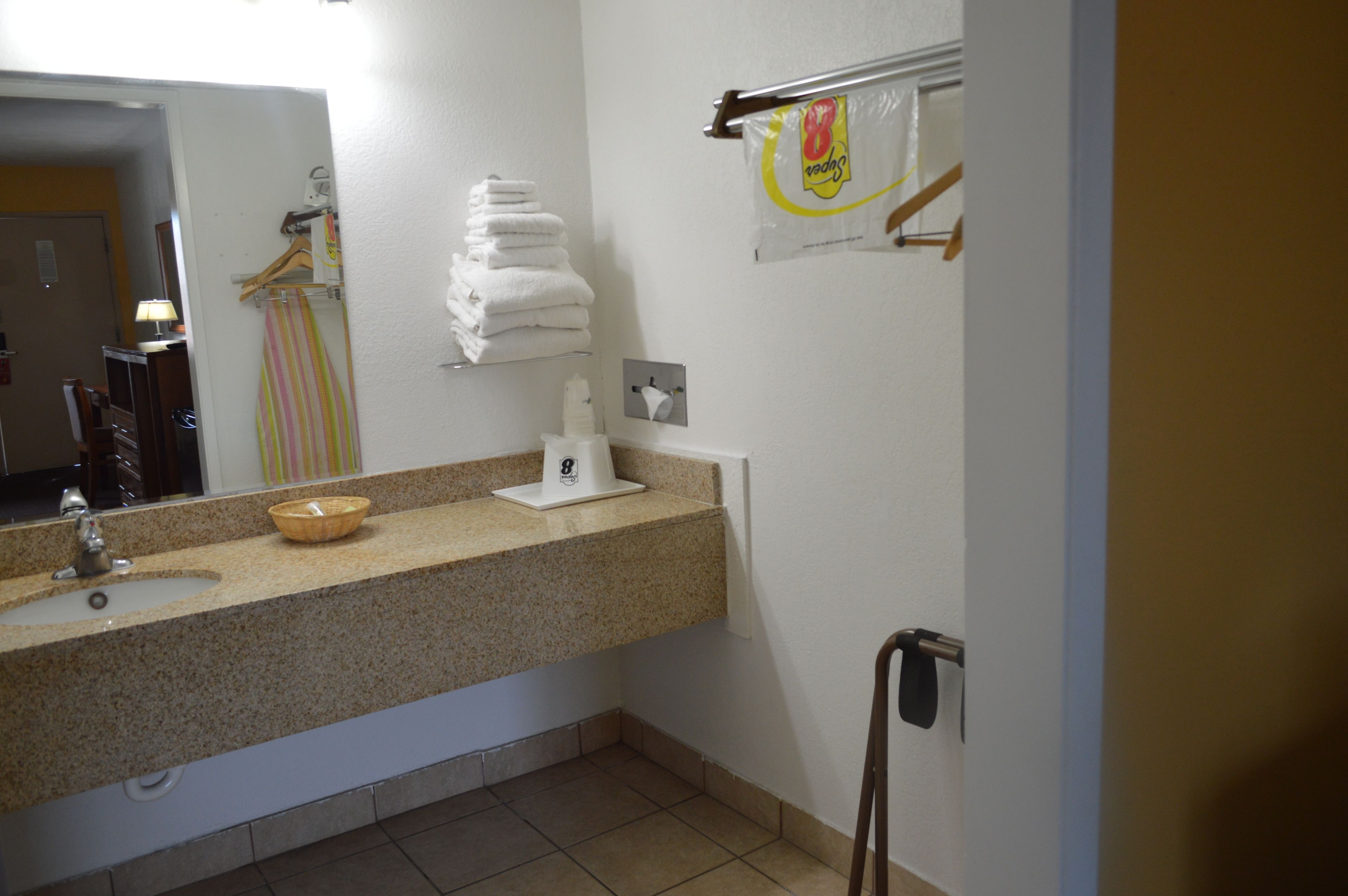 Un baño con lavamanos, espejo, toallero y dispensador de papel higiénico.