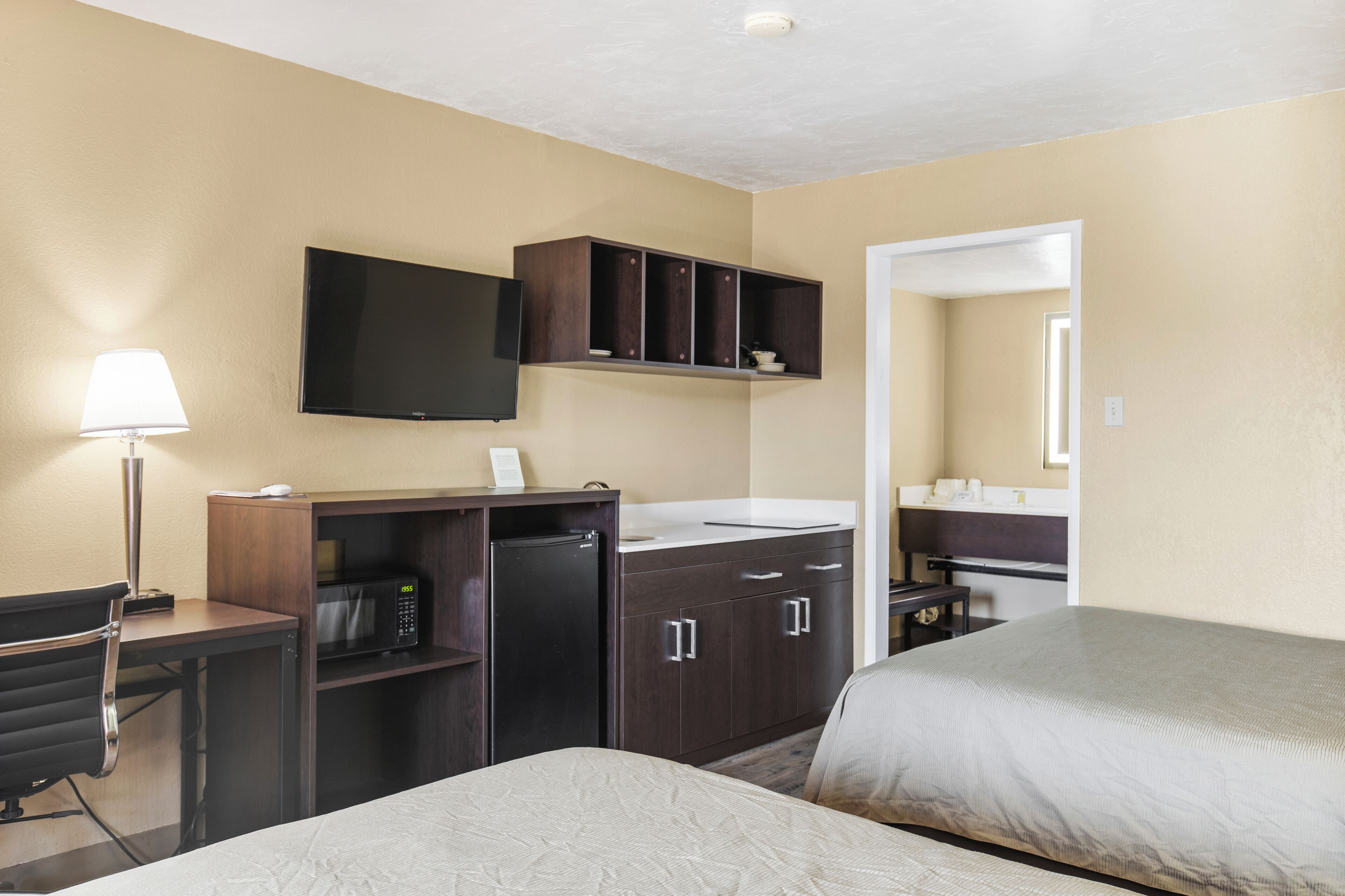 A hotel room with two beds, a desk with a lamp, a microwave, a refrigerator, a television, and a small cabinet.