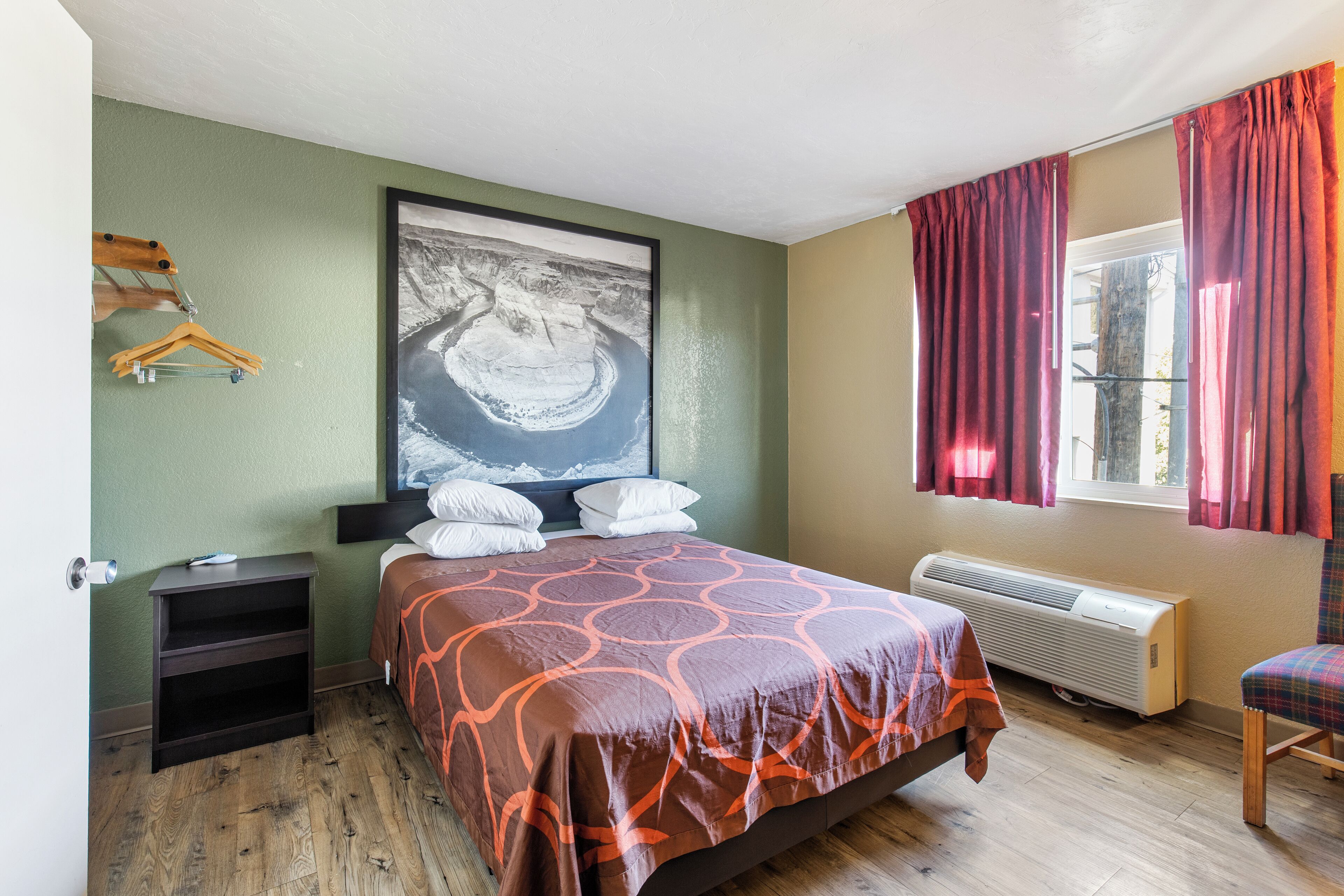 A bedroom with a bed, a nightstand, a heater, a chair, and a wall-mounted coat rack.