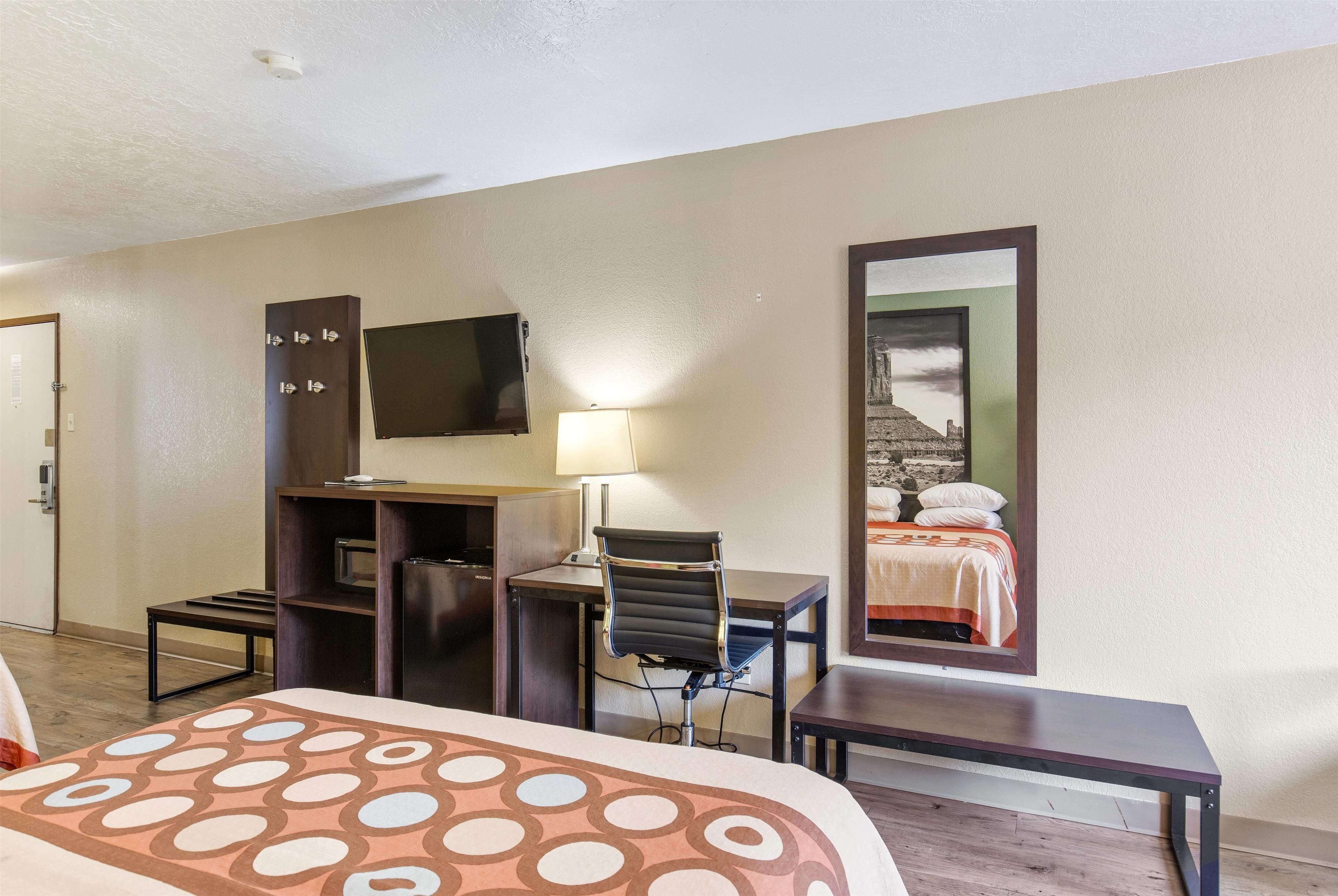 Une chambre d’hôtel équipée d’un lit, d’un bureau, d’une chaise, d’une télévision, d’une lampe et d’un miroir.