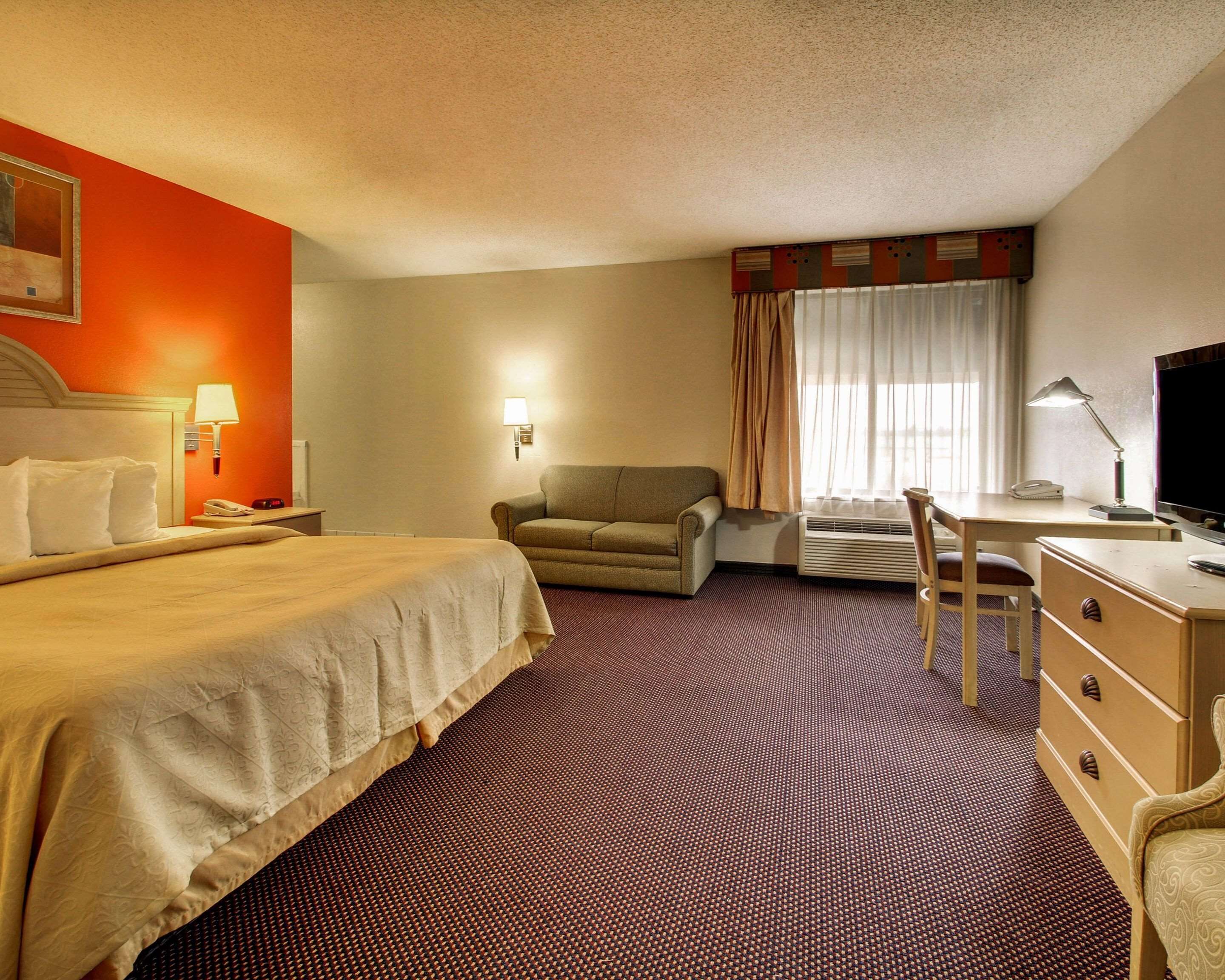 Une chambre d’hôtel comprenant un lit, un canapé, un bureau avec une chaise, une télévision et une fenêtre avec des rideaux.