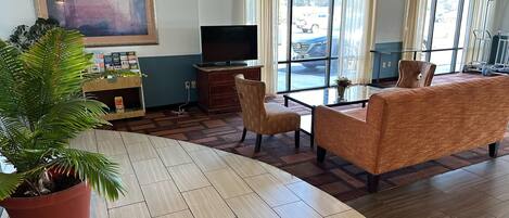 A hotel lobby with a large potted plant, a flat-screen TV, a sofa, and a coffee table.