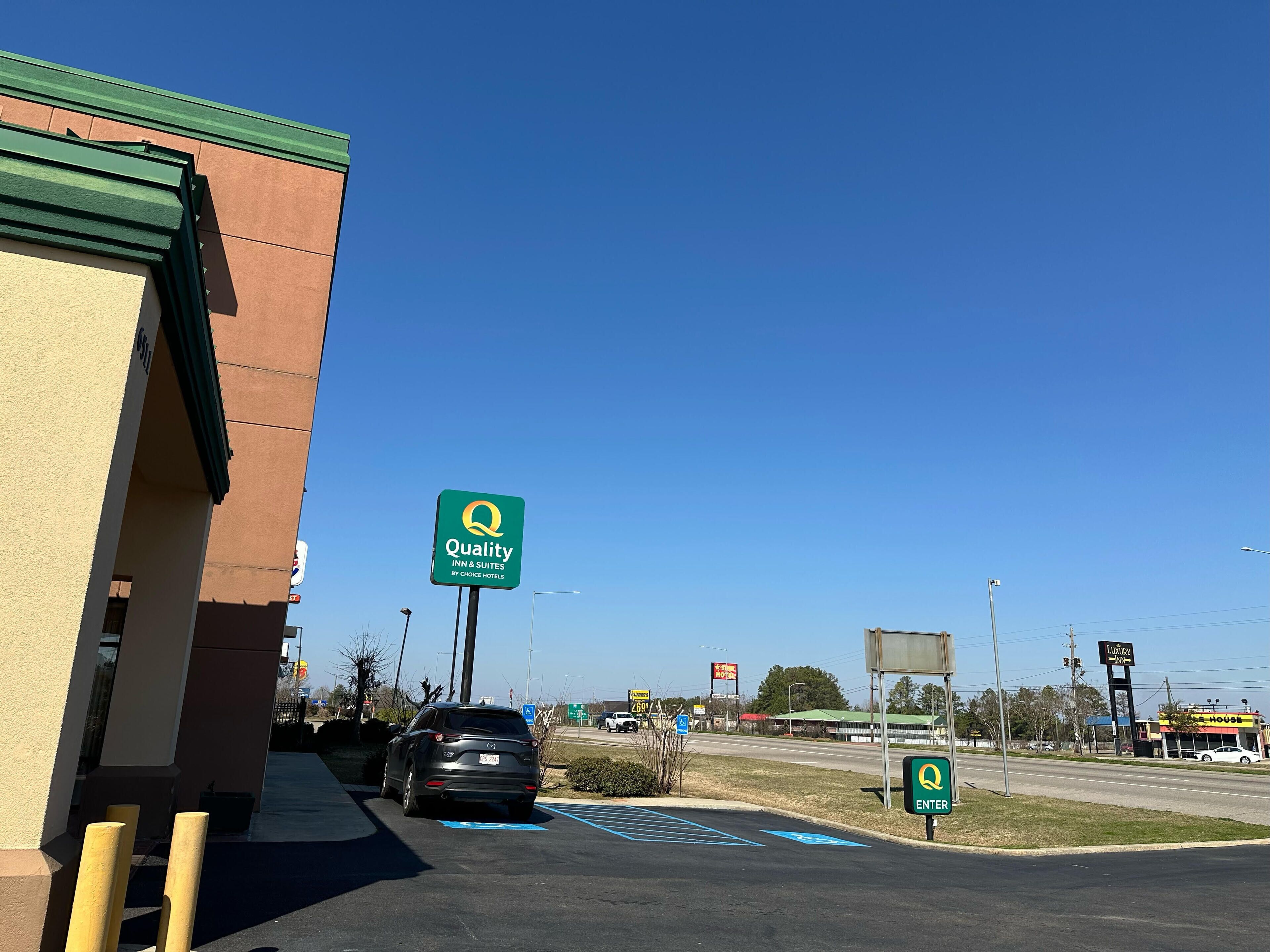 A Quality Inn & Suites sign, a parking lot, and a building with a green roof.