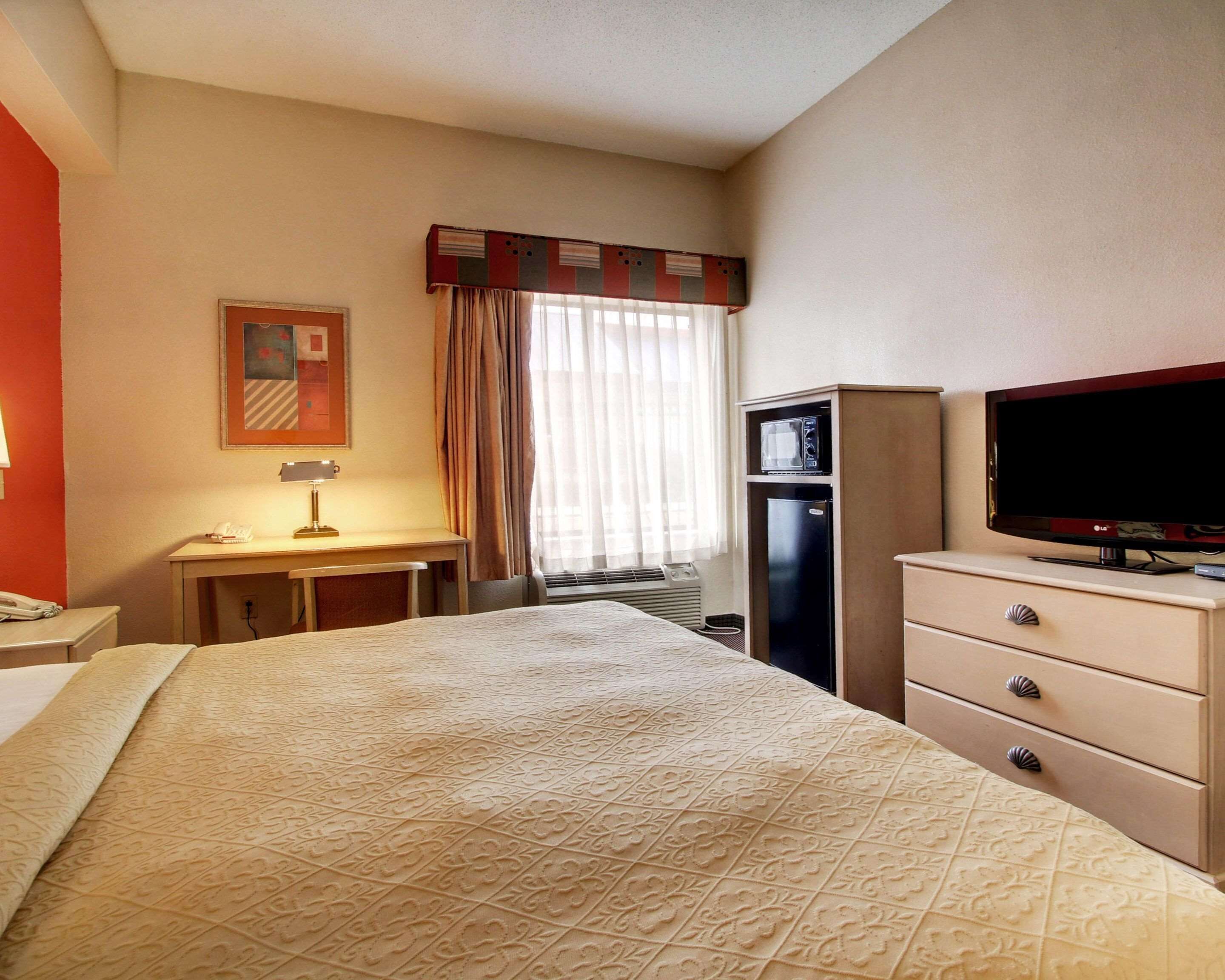 A hotel room with a bed, a desk, a television, a minibar, and a window with curtains.