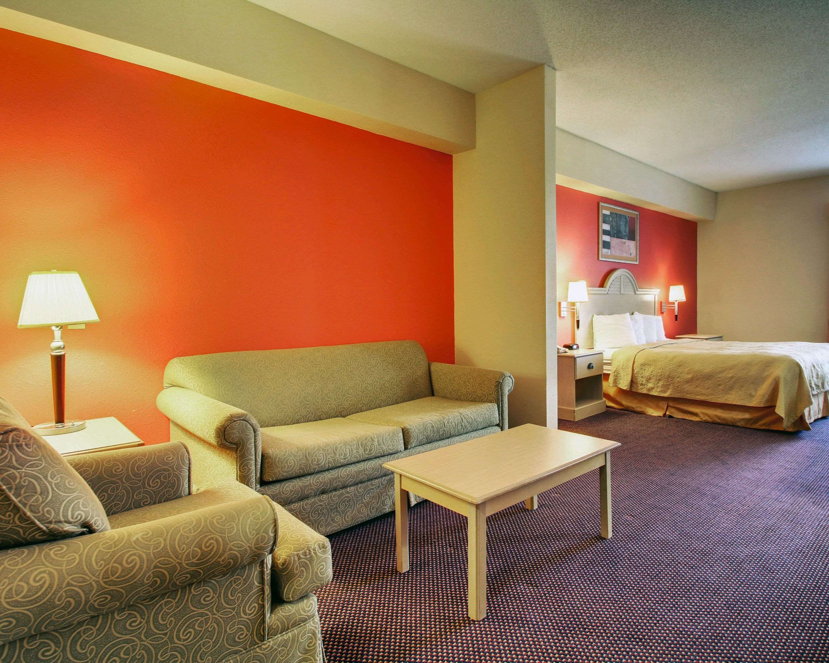 A hotel room with a sofa, a small table, a bed, and a nightstand with a lamp.