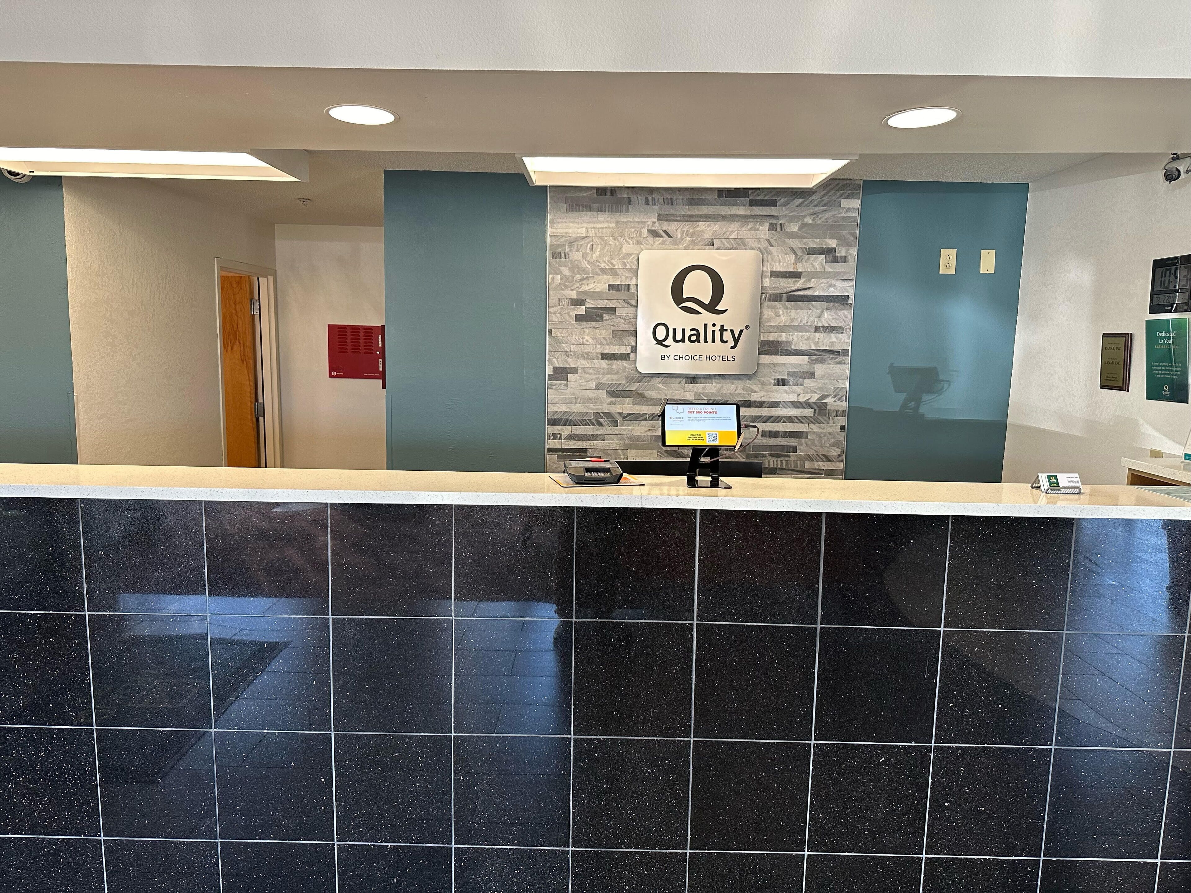 A hotel reception area with a modern design, featuring a reception desk, a digital screen, and a sign that reads "Quality by Choice Hotels".