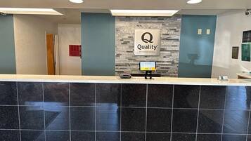 Zona de recepción de un hotel con diseño moderno, que incluye un mostrador de recepción, una pantalla digital y un cartel que dice "Quality by Choice Hotels".