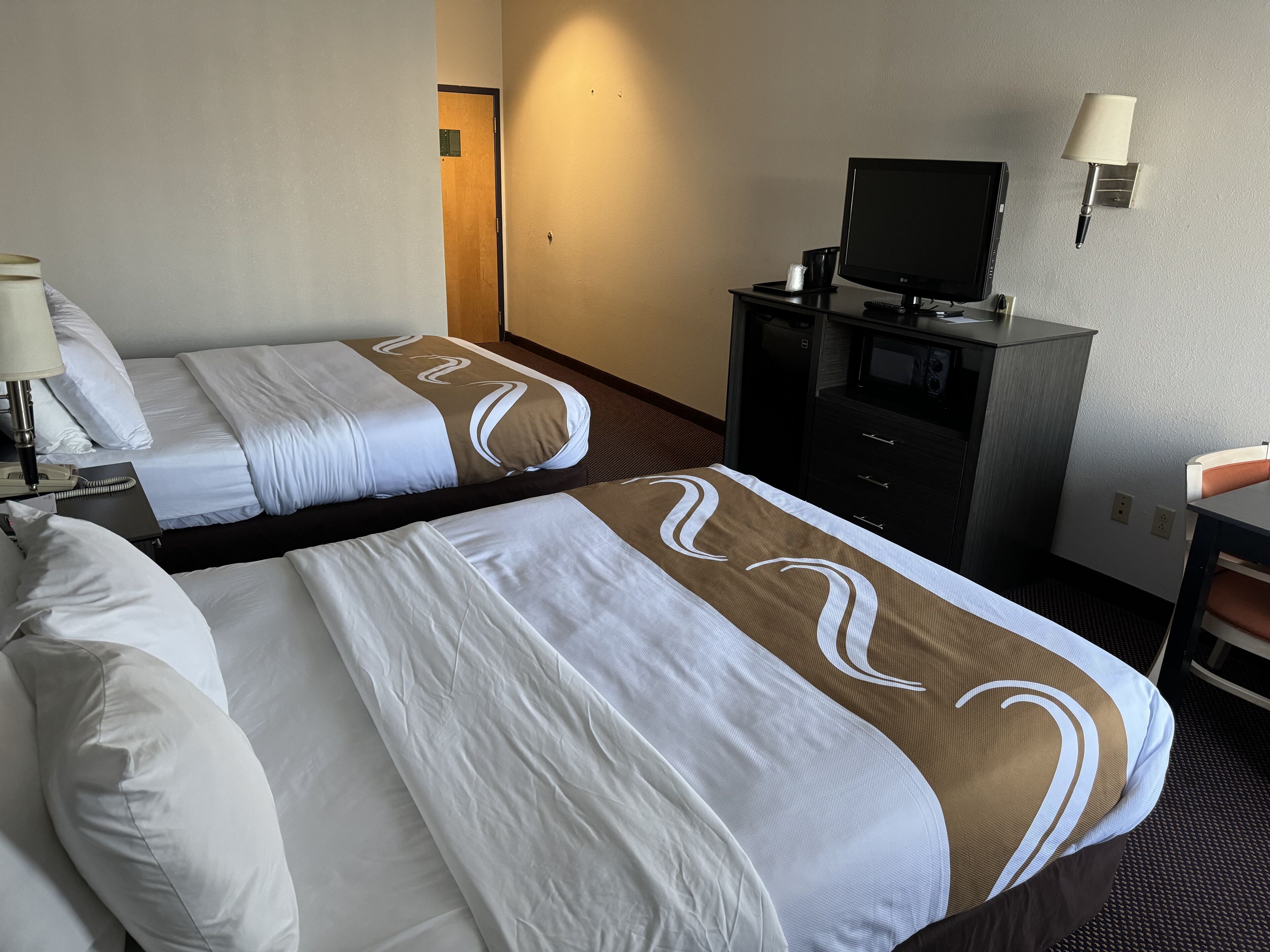Een hotelkamer met twee bedden, een televisie, een bureau en een lamp.