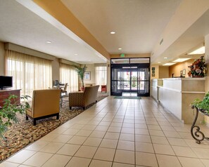 A hotel lobby with a reception desk, a seating area with a sofa and chairs, a television, and a plant. - Quality Inn &  Suites Hattiesburg North (Hattiesburg)
