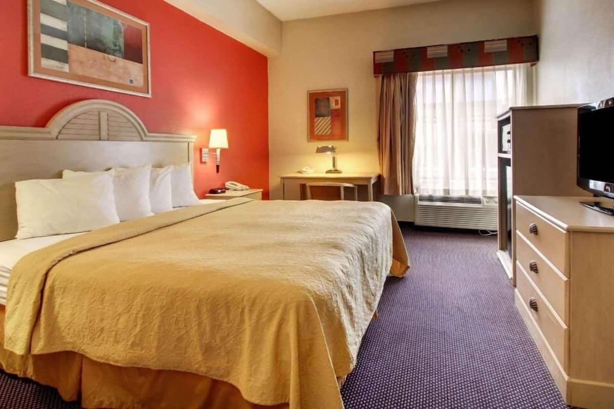 Een hotelkamer met een bed, een bureau, een televisie en een raam met gordijnen.