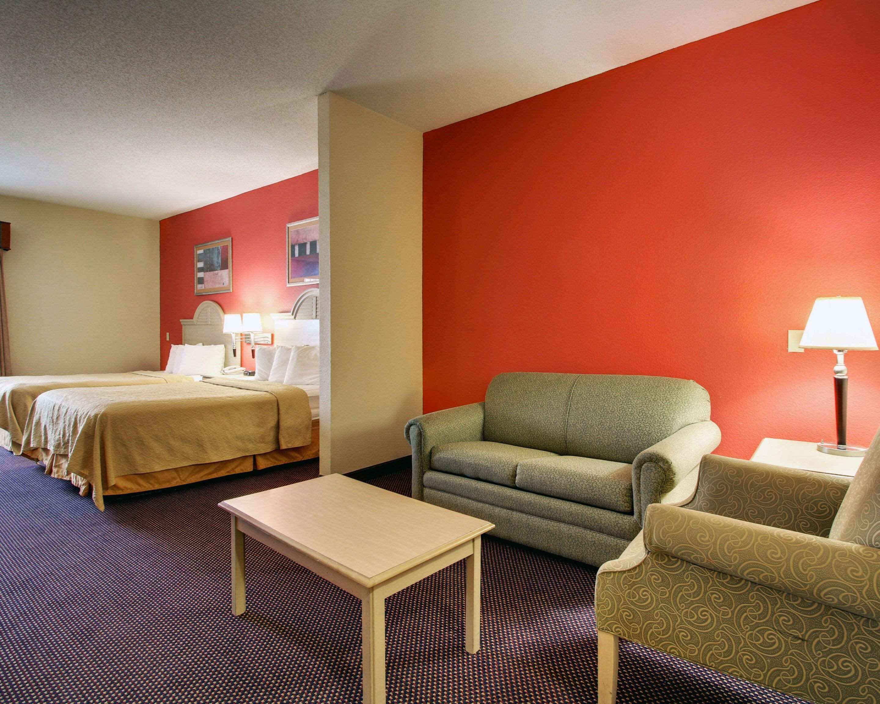 Una habitación de hotel con dos camas, un sofá, una mesita y una lámpara.